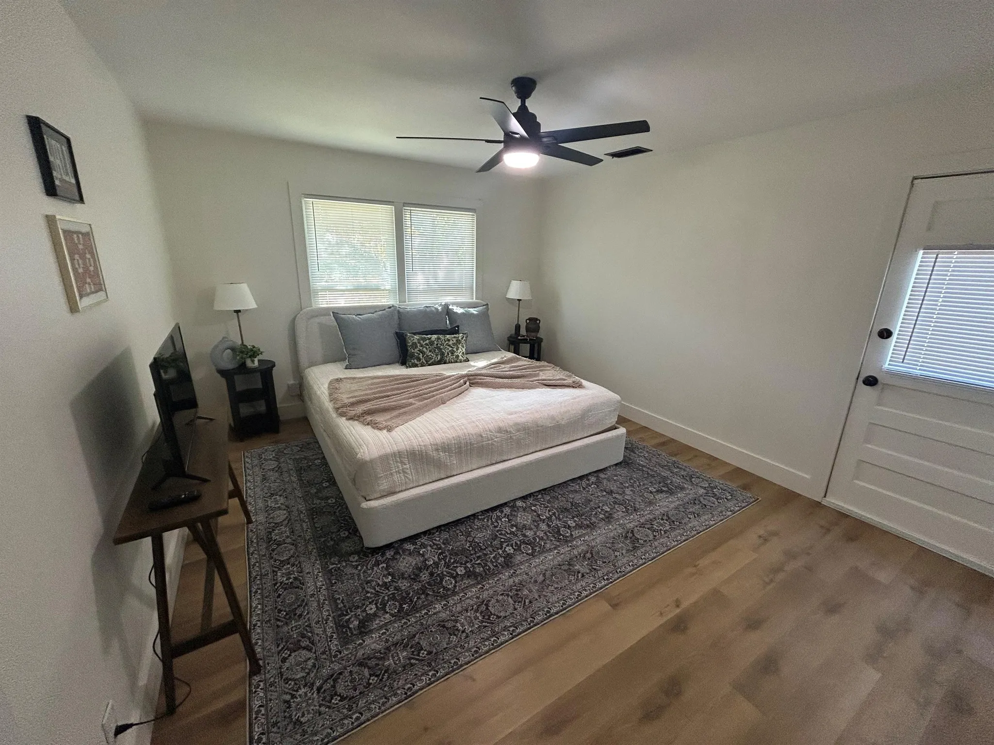 A bedroom with a bed, ceiling fan, TV, and framed pictures on the wall.
