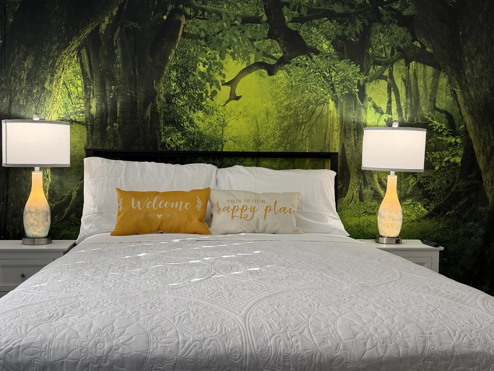 A bed with a forest mural, white bedding, and two bedside lamps.