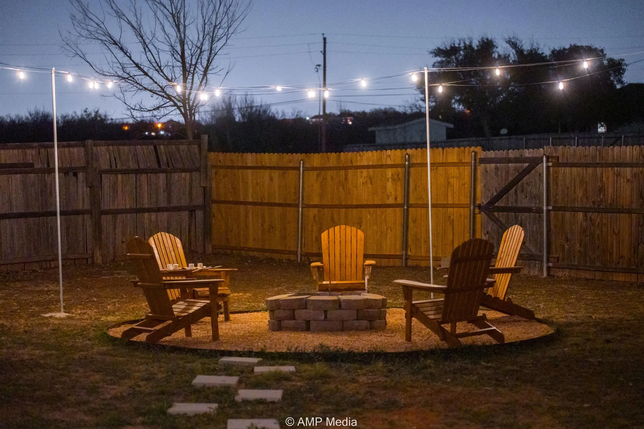 Backyard with string lights, Adirondack chairs, and a fire pit at dusk.