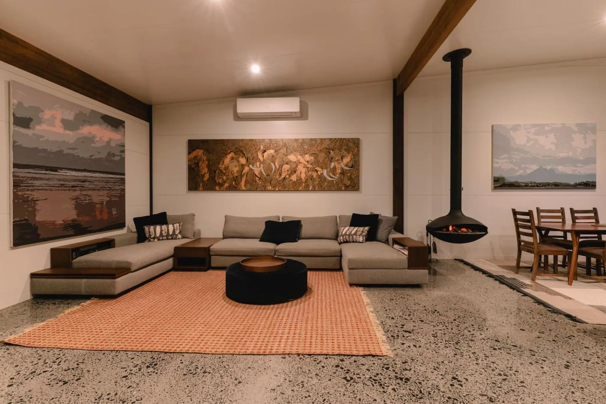 Living room with sectional sofa, fireplace, dining table, and large artwork.