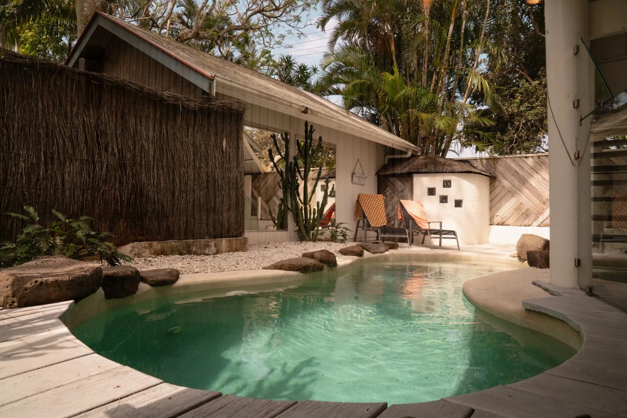 An outdoor pool with lounge chairs and a thatched-roof building.