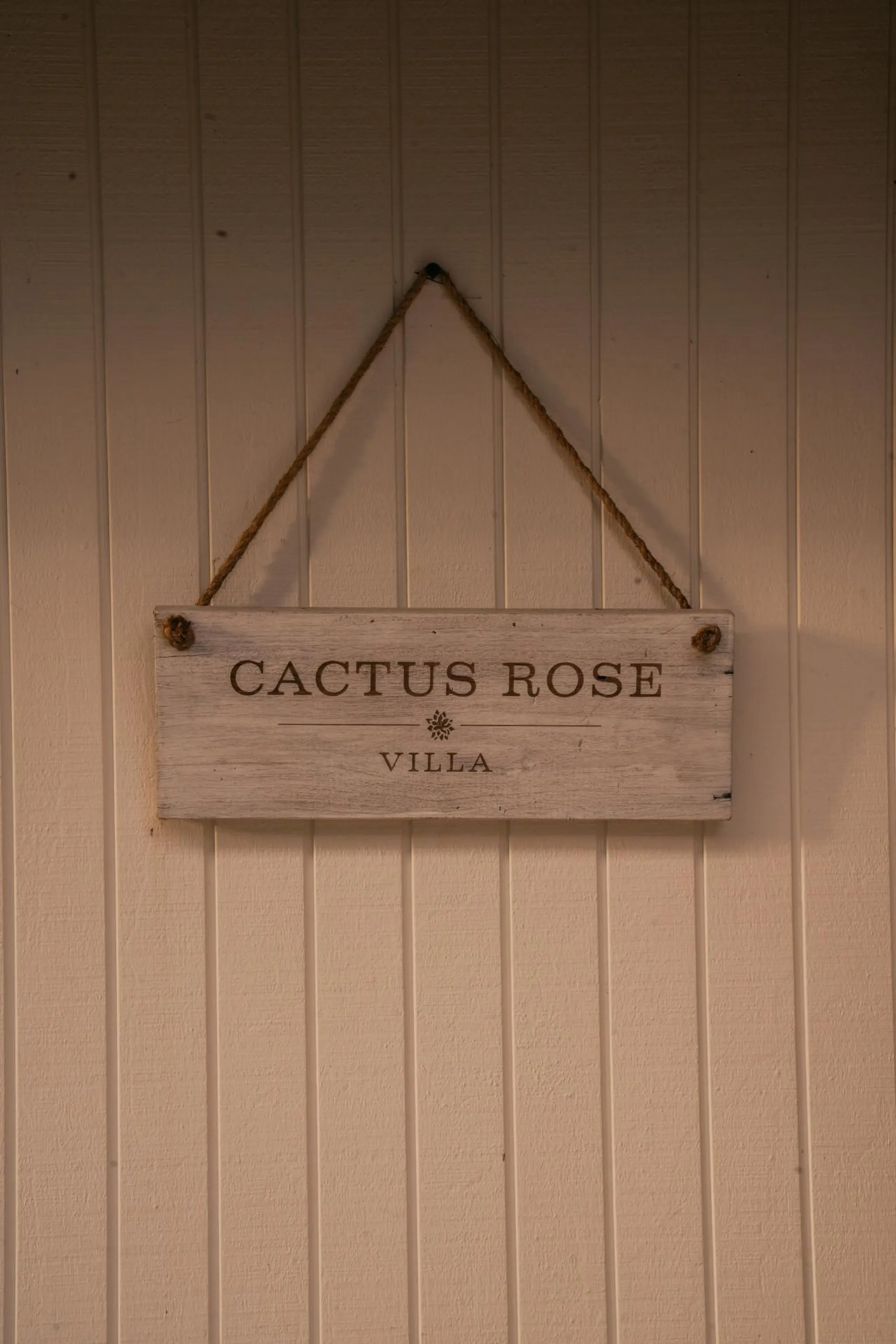 A white wooden sign with "CACTUS ROSE VILLA" is hanging on a light brown wall.