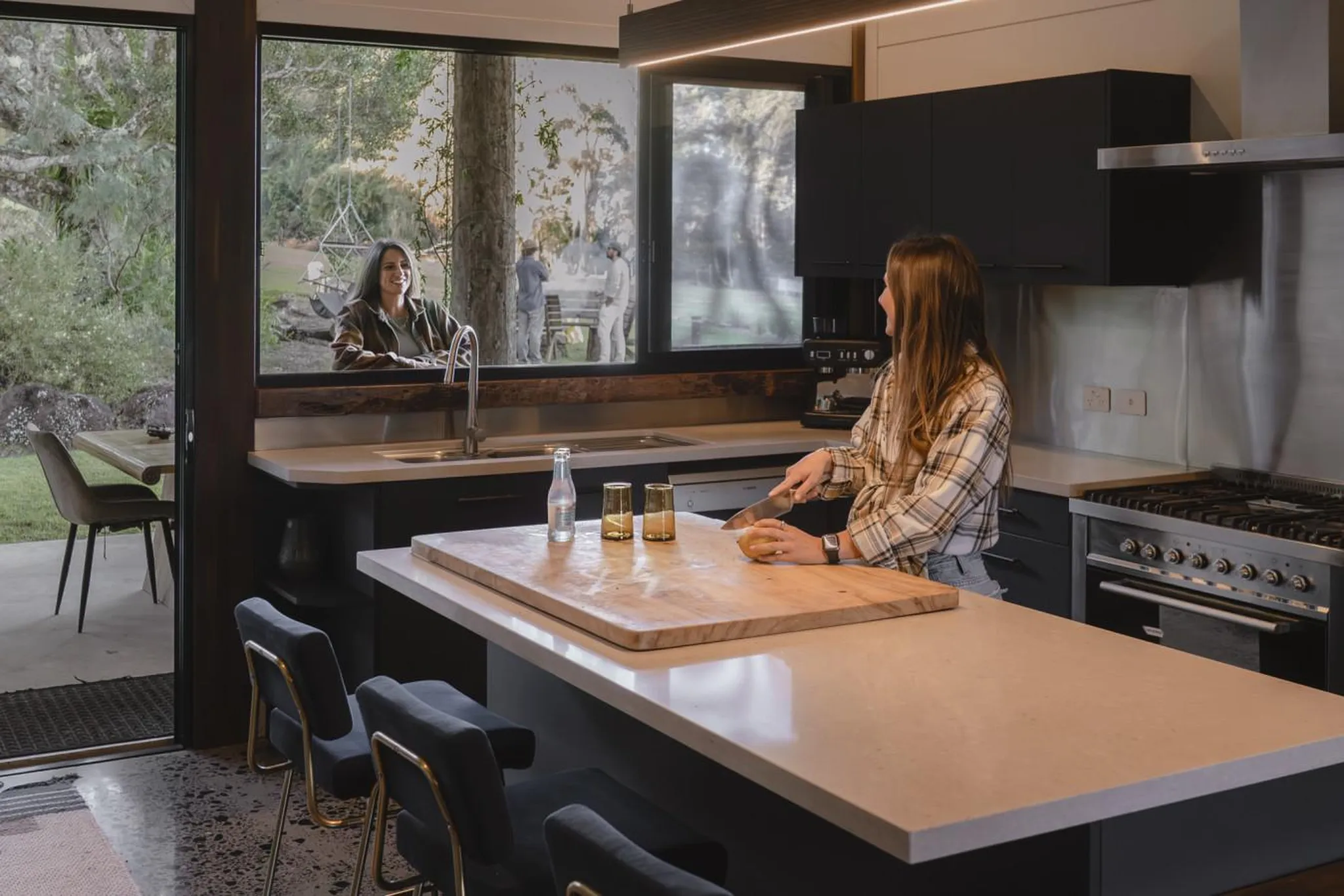 Woman in plaid shirt cutting potato in modern kitchen with large window.