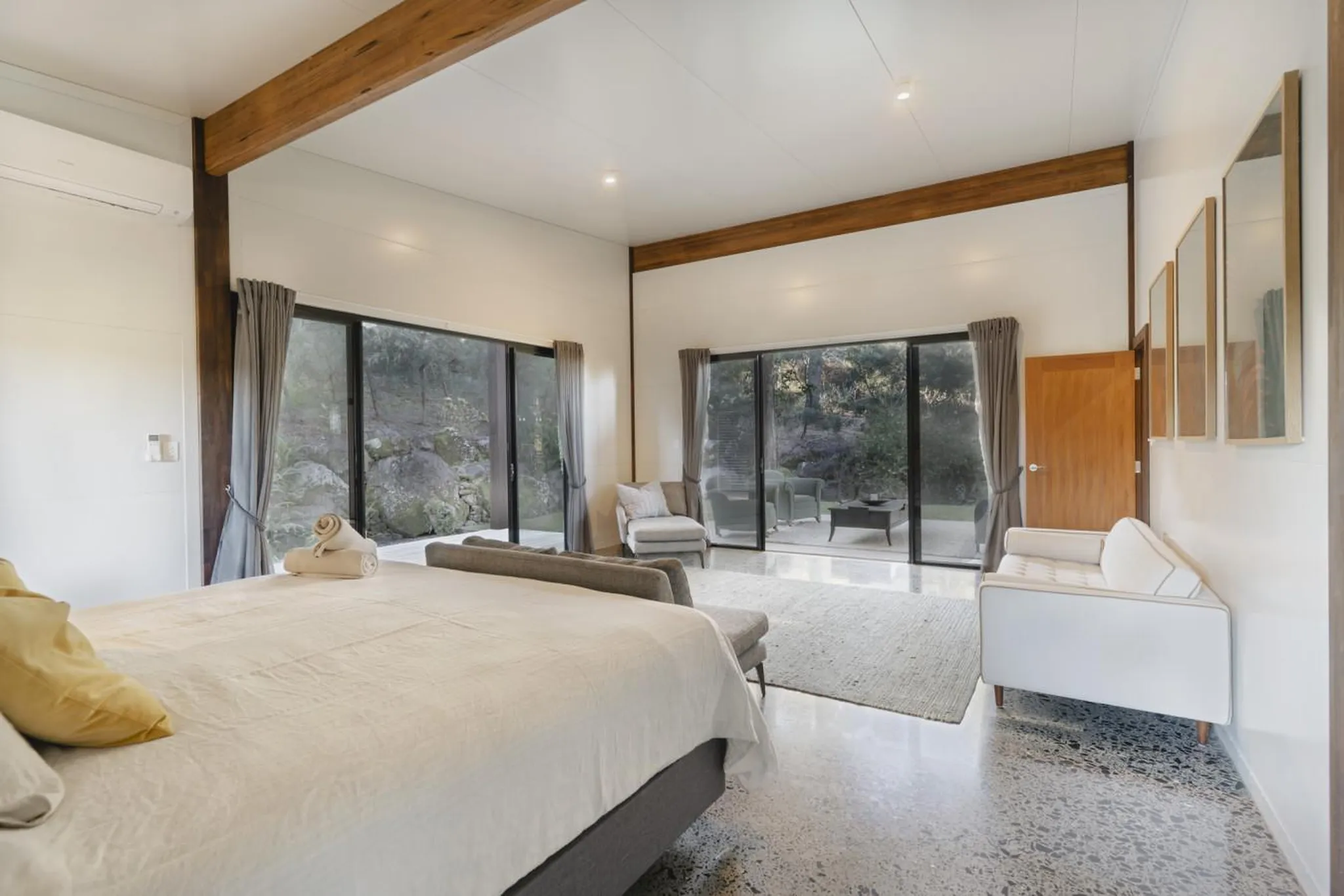 Interior of a bedroom with large windows overlooking a rocky, forested landscape.