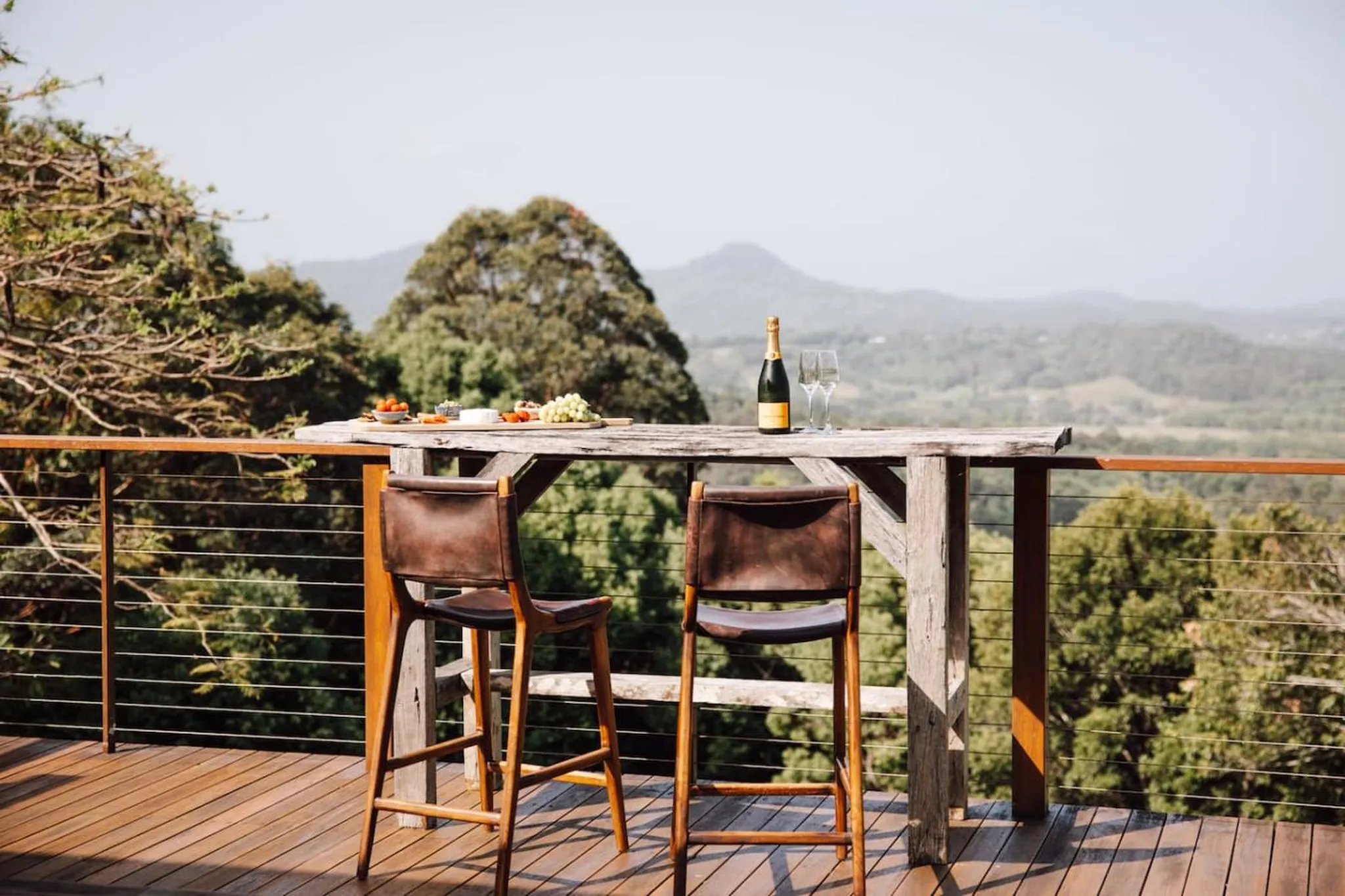 A romantic outdoor setting with champagne and a cheese board on a wooden table with two chairs.