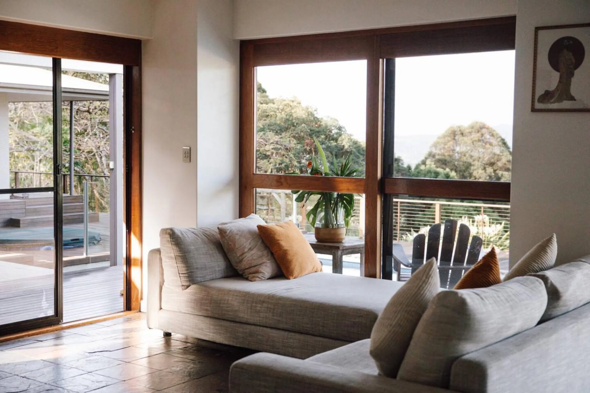 A living room with large windows overlooking a forest and a grey sofa with pillows.
