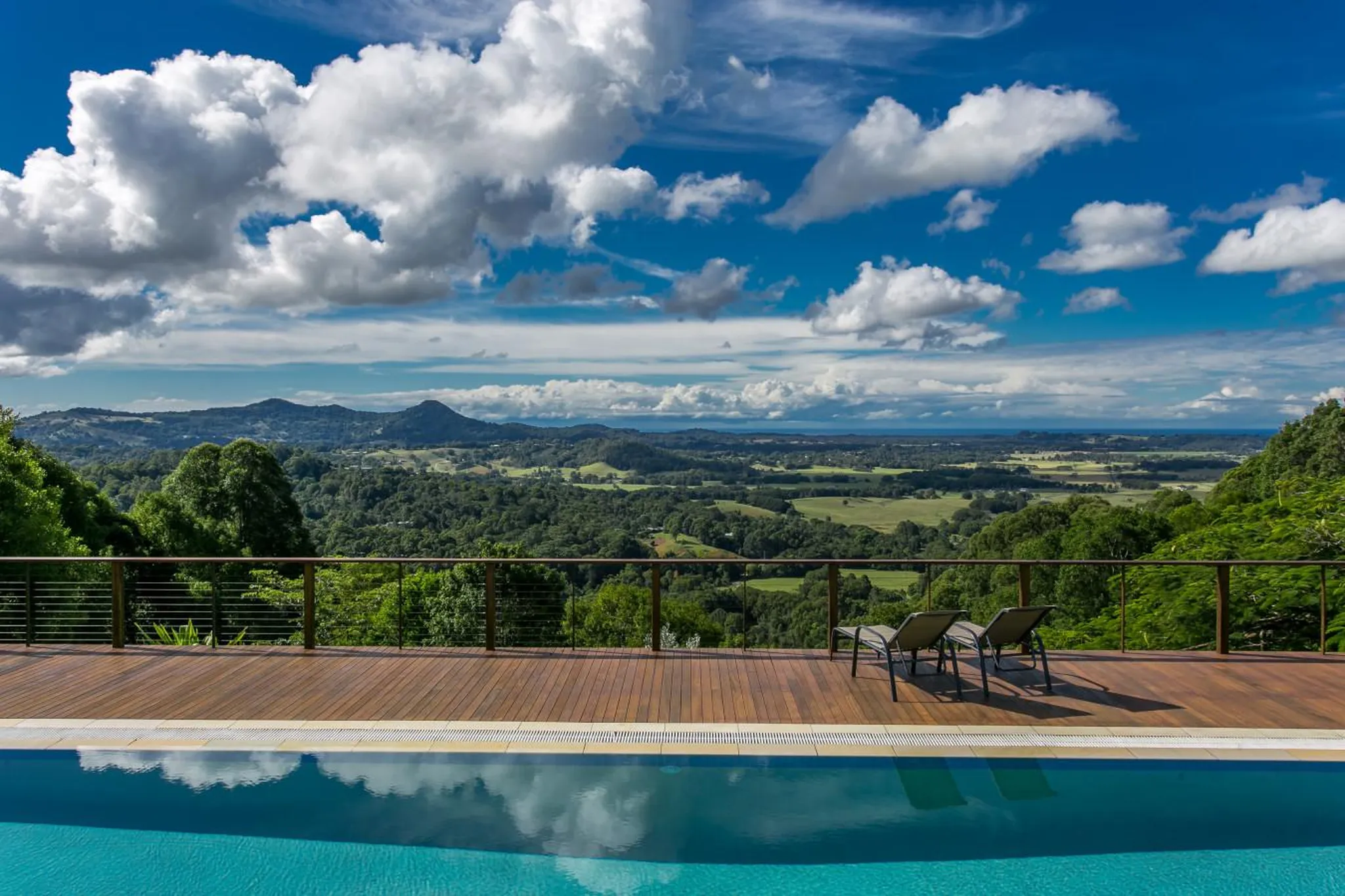 Luxury infinity pool with stunning rolling green hills and a blue sky with clouds.