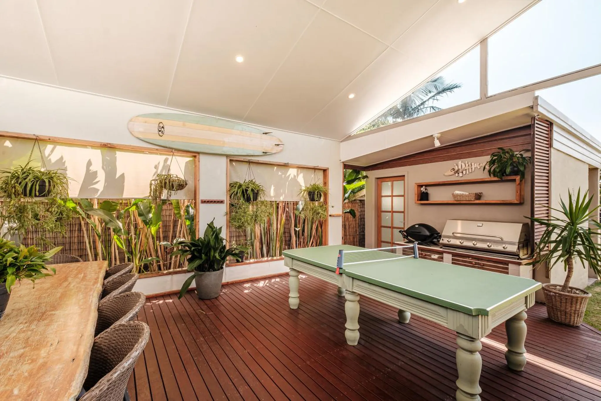 Outdoor patio with a ping pong table, grill, and lush greenery.