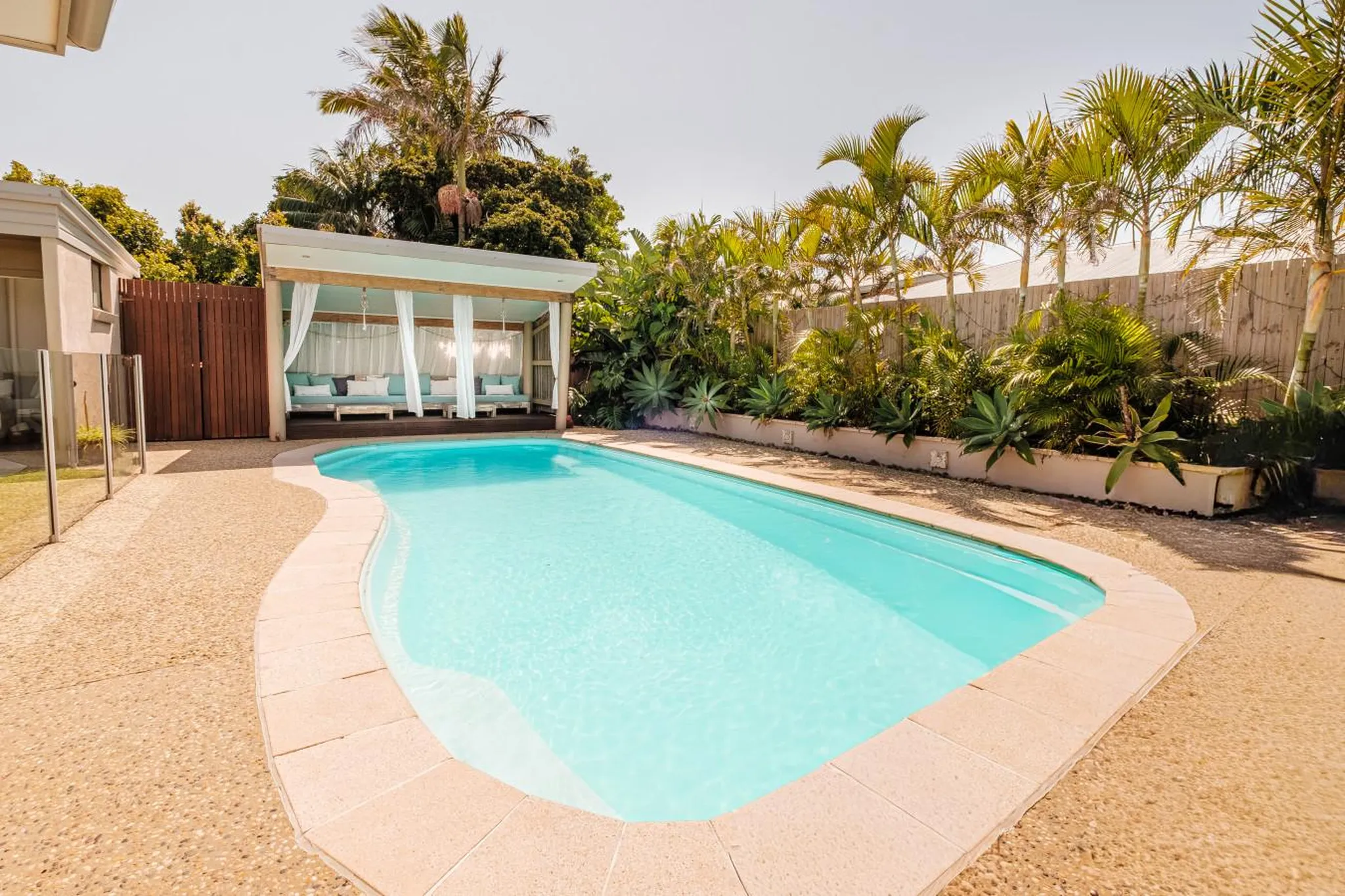 A bright blue pool with a cabana and palm trees.