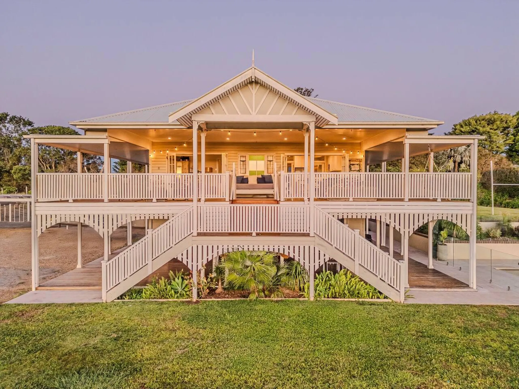 Large Queenslander-style house with wraparound verandas, wide stairs, and a grassy yard.