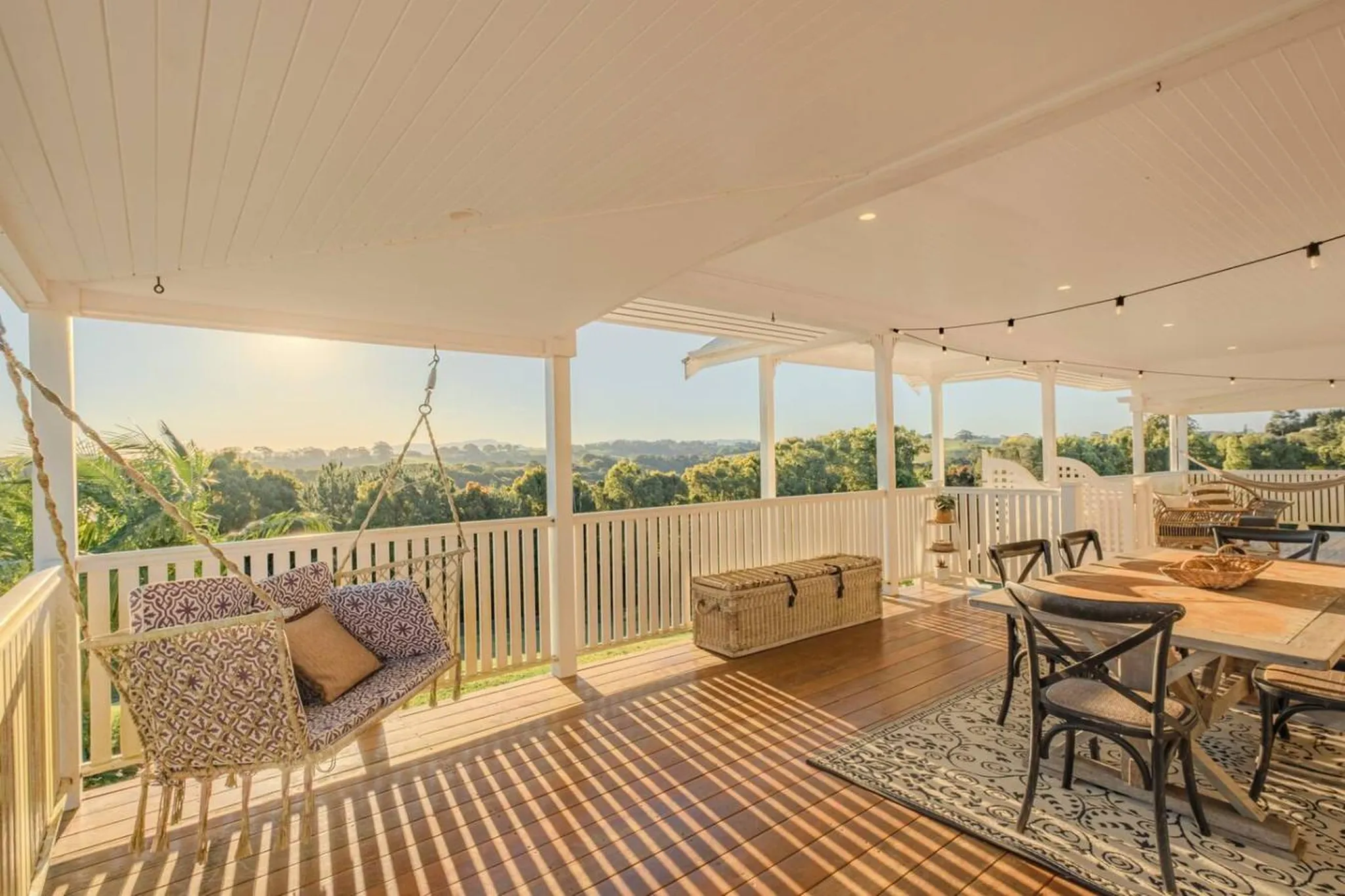 A sun-drenched patio with a swinging chair and dining set overlooking a lush landscape.