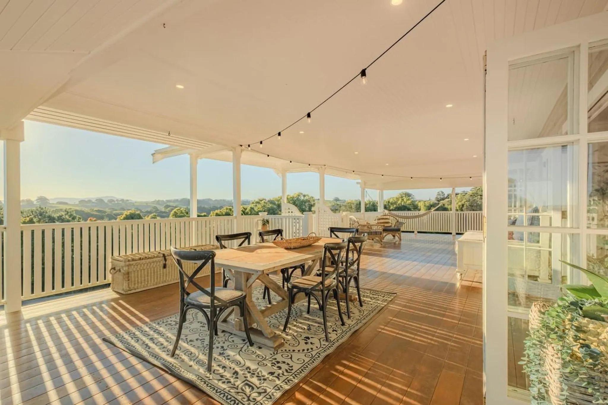A covered deck with a dining table, chairs, and a hammock overlooking a scenic landscape.