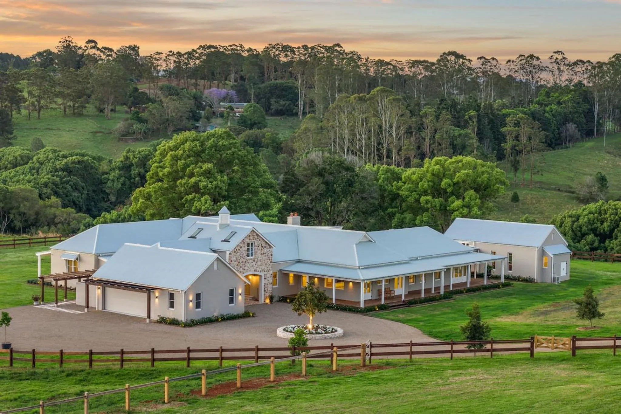 Luxury estate home with metal roof and stone accents surrounded by lush green hills.