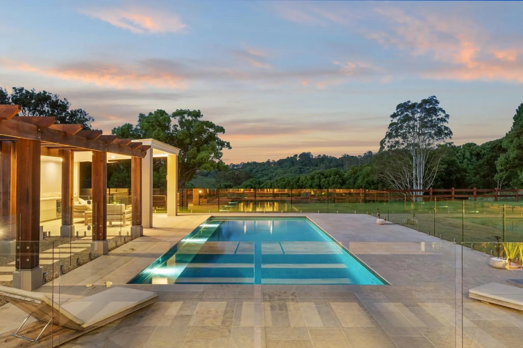 Luxury resort pool at dusk with pergola and lounge chairs.