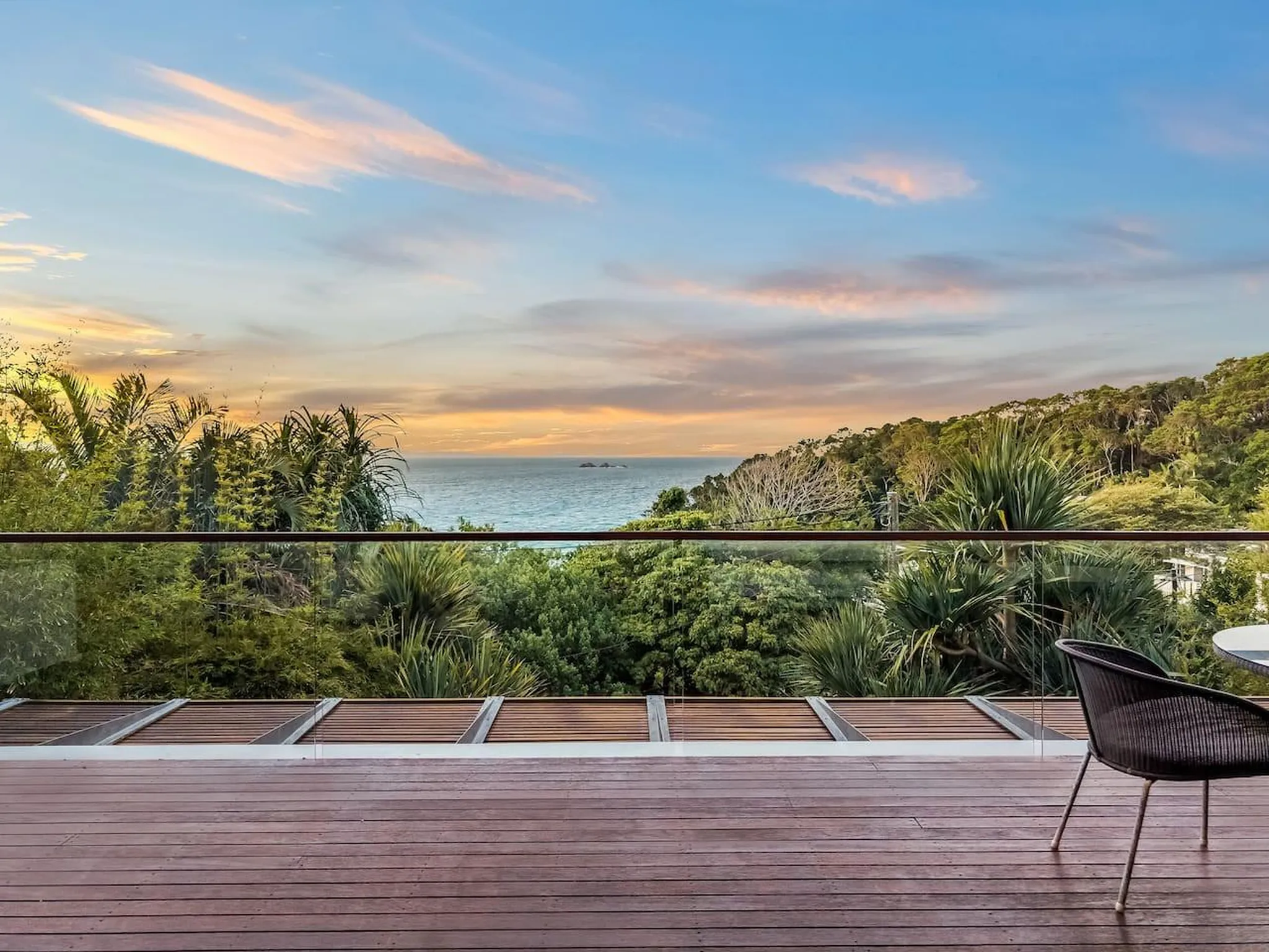 A deck overlooking lush greenery and the ocean at sunset.