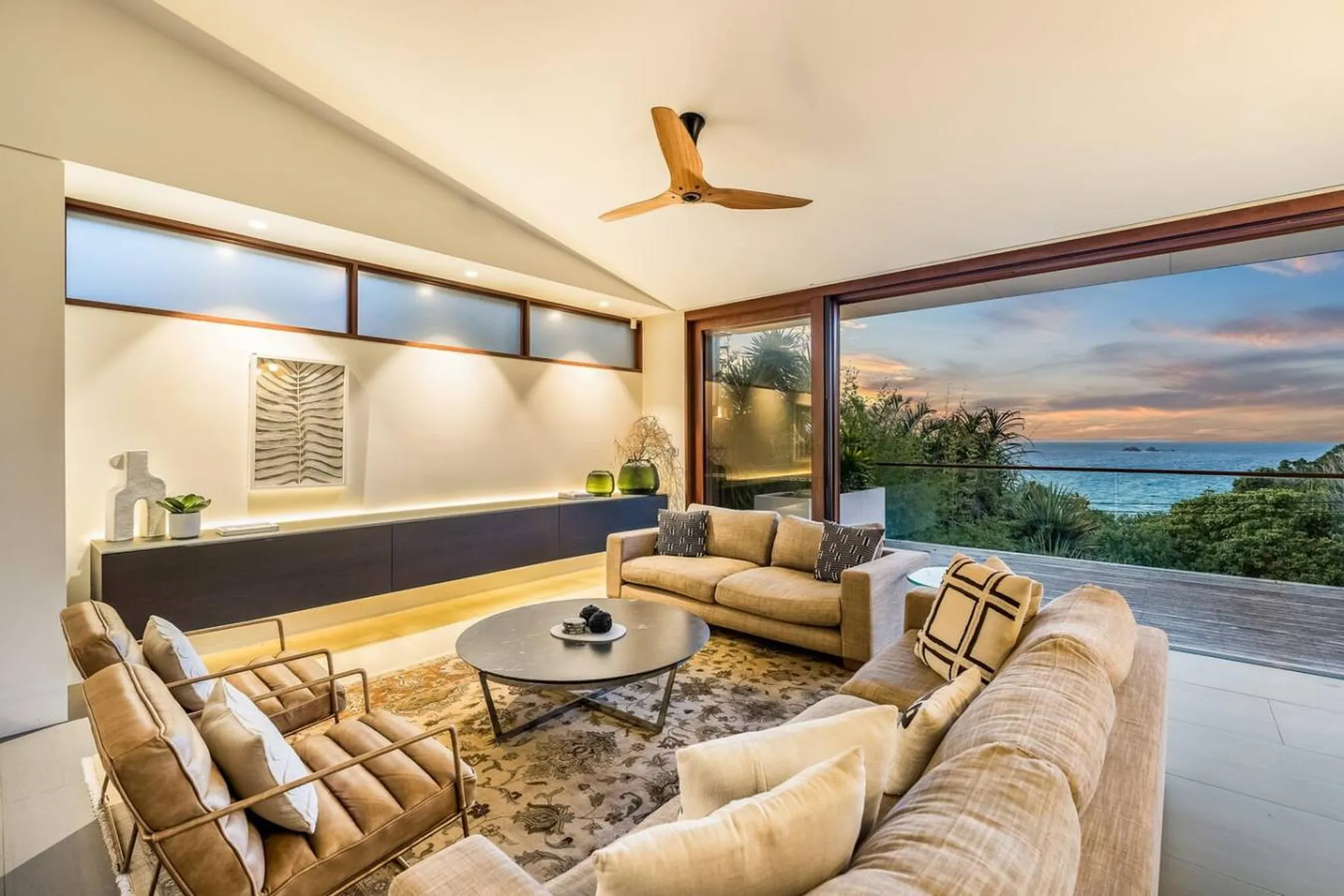 A modern living room with a large window overlooking the ocean at sunset.