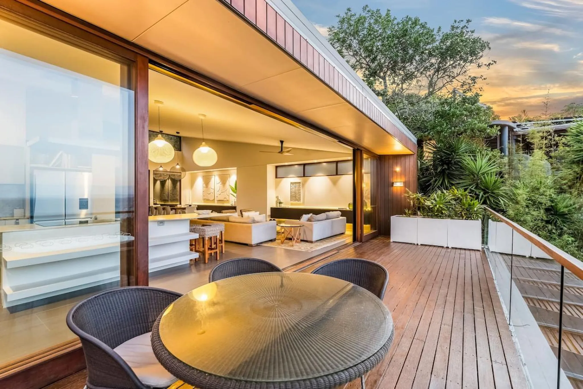 An open-plan kitchen and living area with large glass doors leading to a wooden deck with a dining t