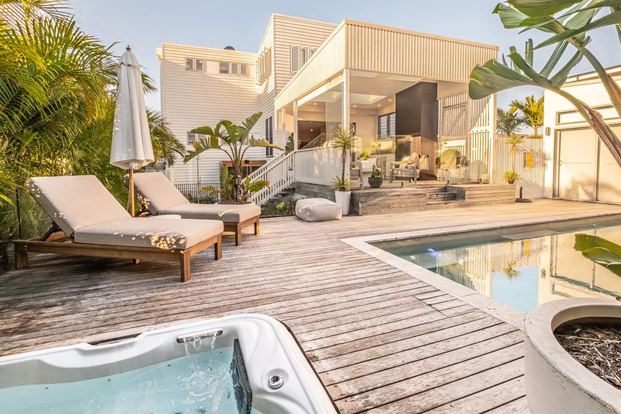 Outdoor hot tub and swimming pool with lounge chairs and a modern house.
