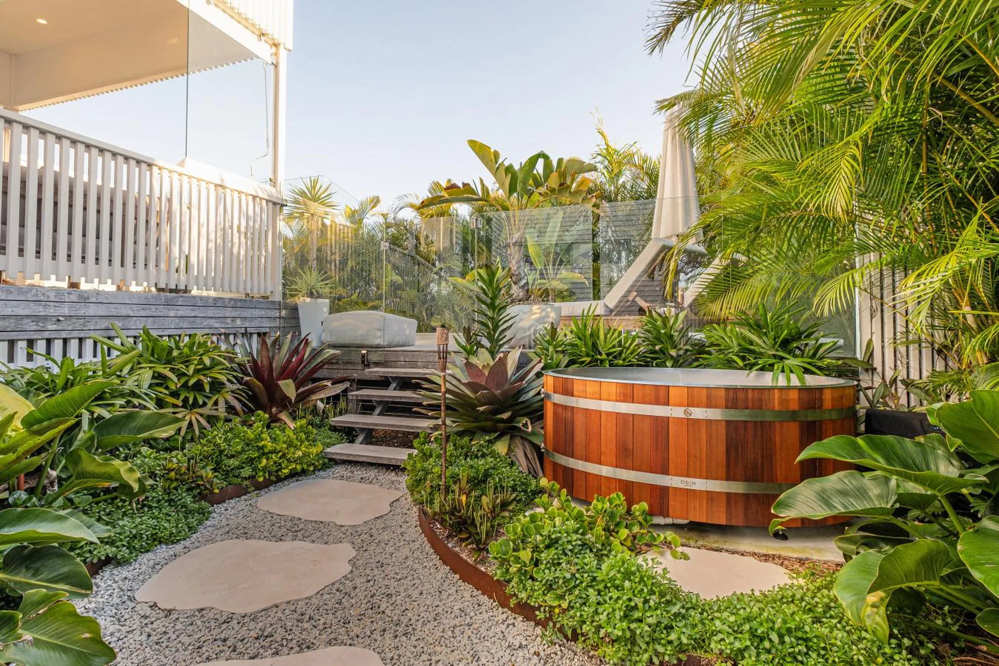 An outdoor deck with a wooden hot tub and lush tropical plants.