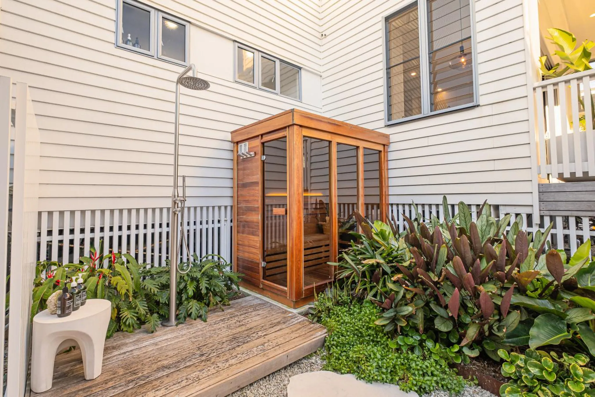 Outdoor wooden sauna with shower and plants.