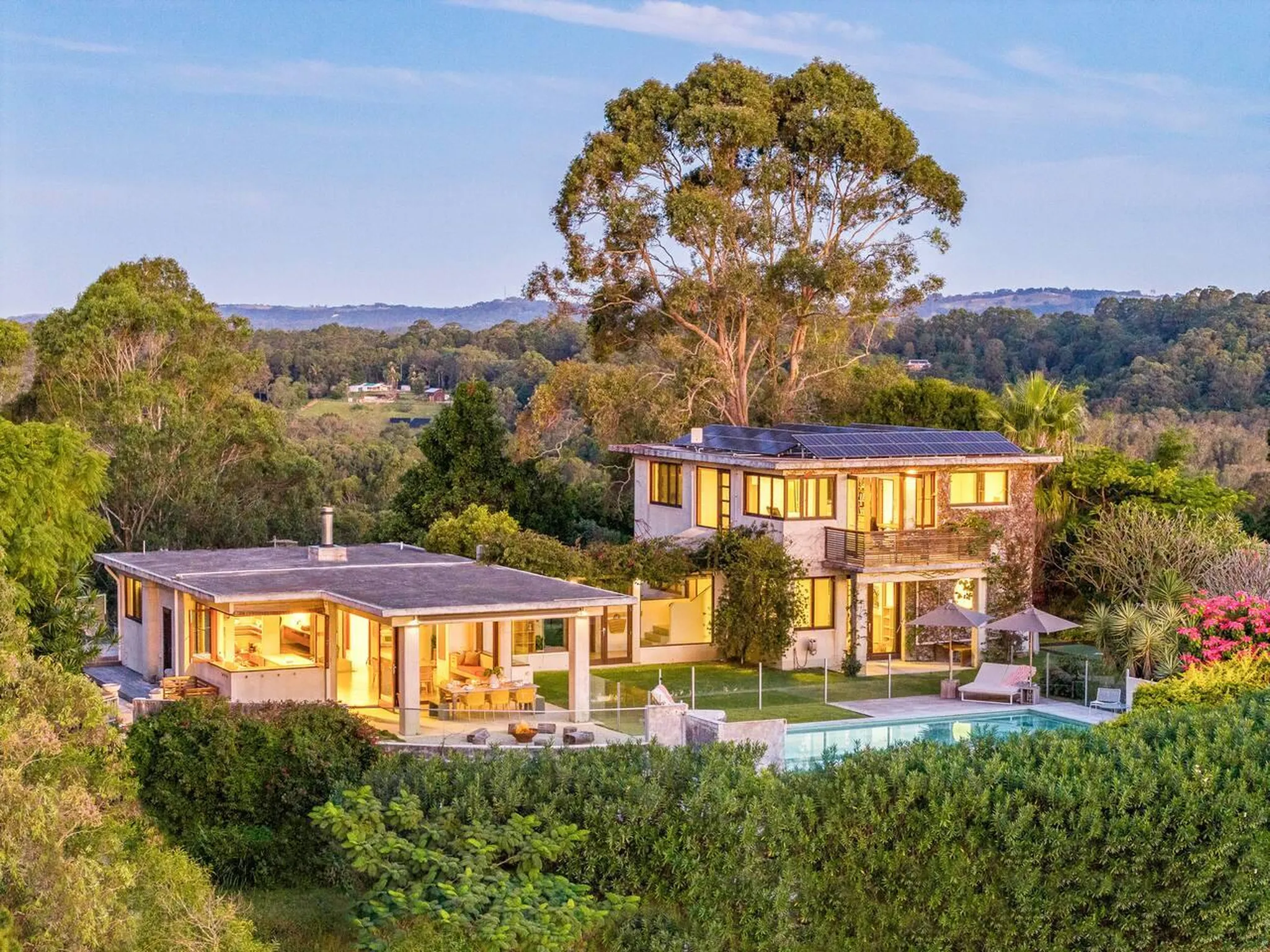 Luxury homes with pool and solar panels in a lush, hilly landscape at sunset.