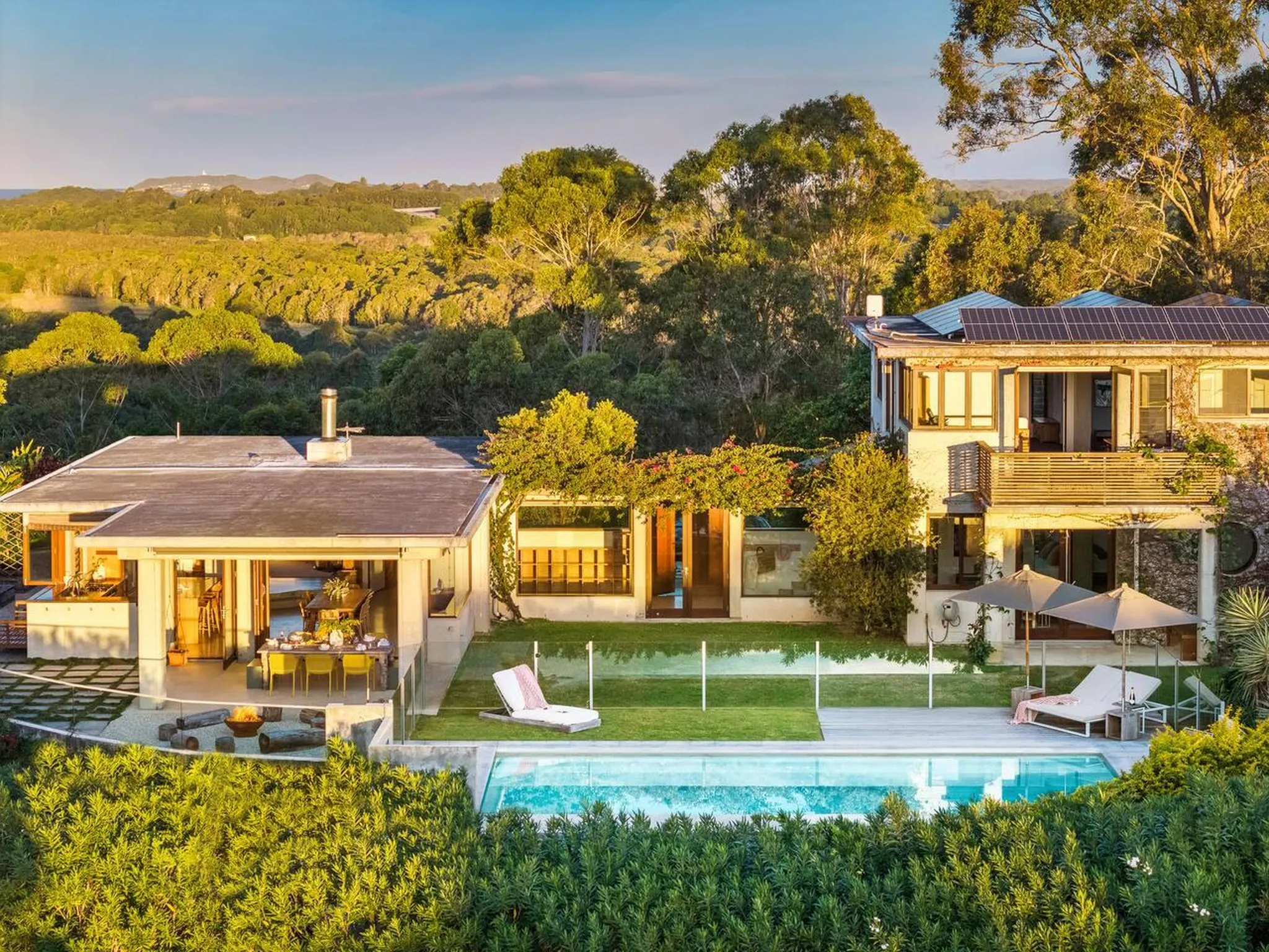 A modern house with a pool and a scenic view of trees and hills at sunset.