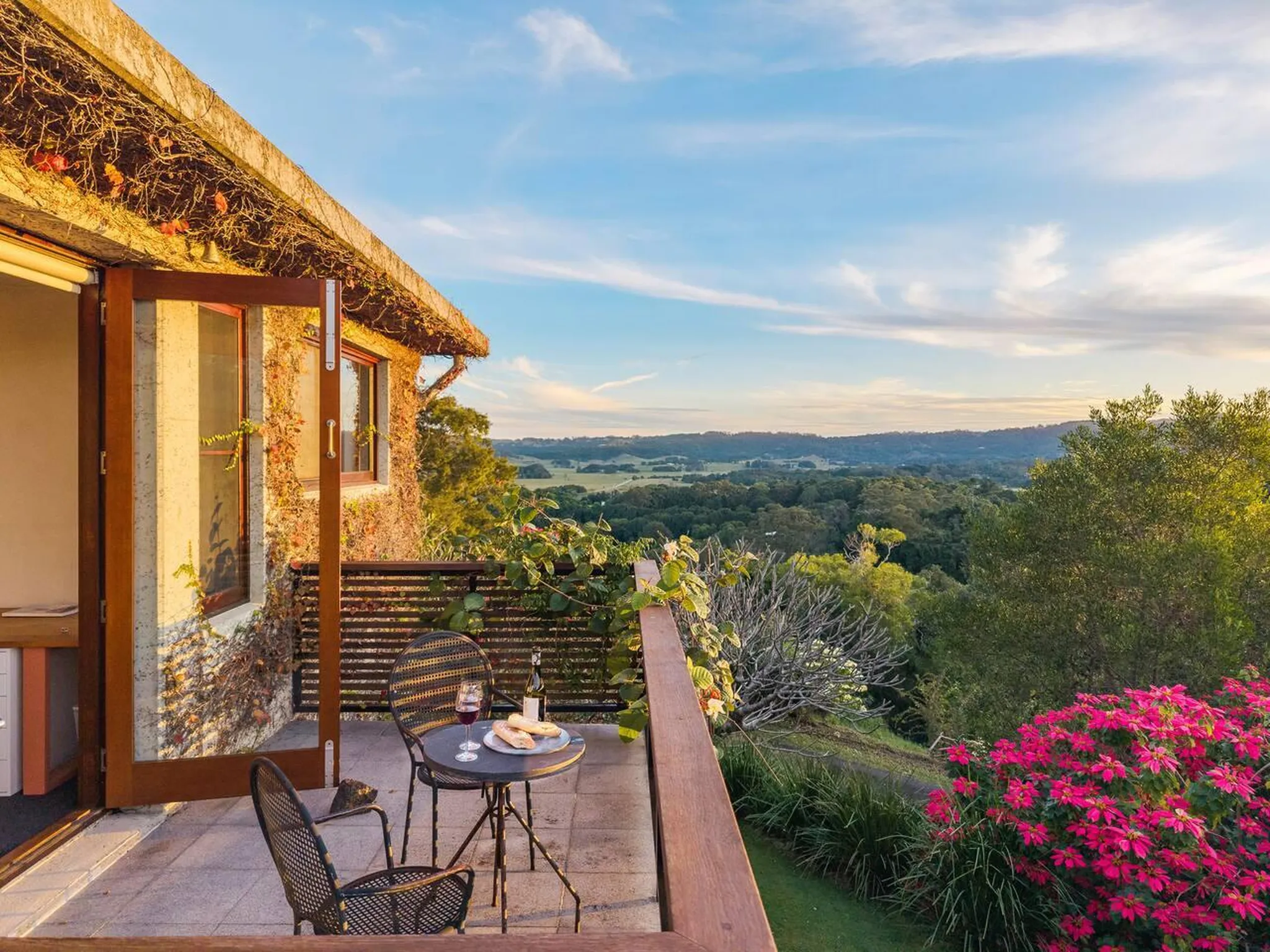 Balcony with a table, chairs, and a glass of wine overlooking a scenic landscape.