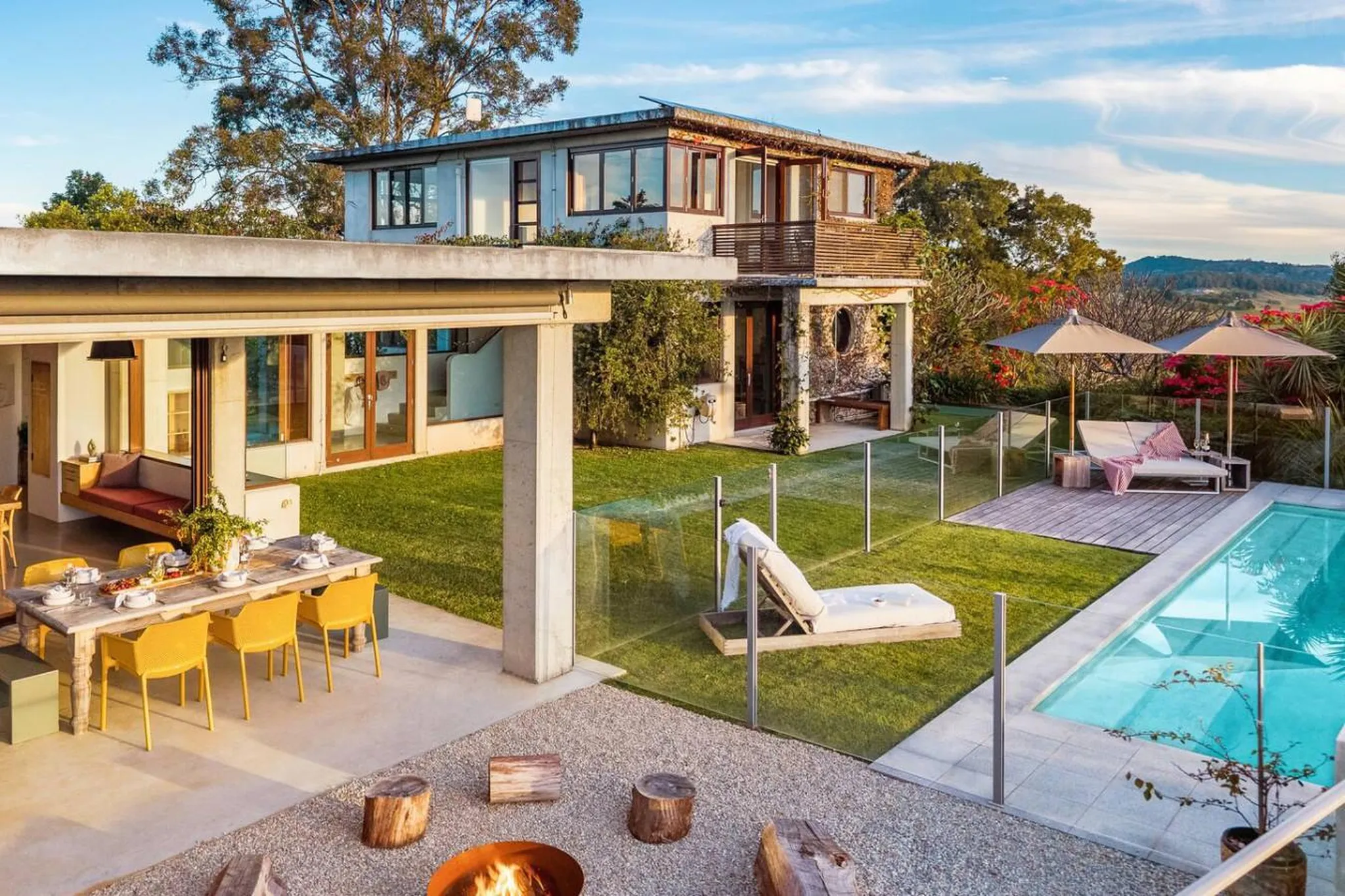 Luxury outdoor living area with pool, lounge chairs, dining table, and a modern house.
