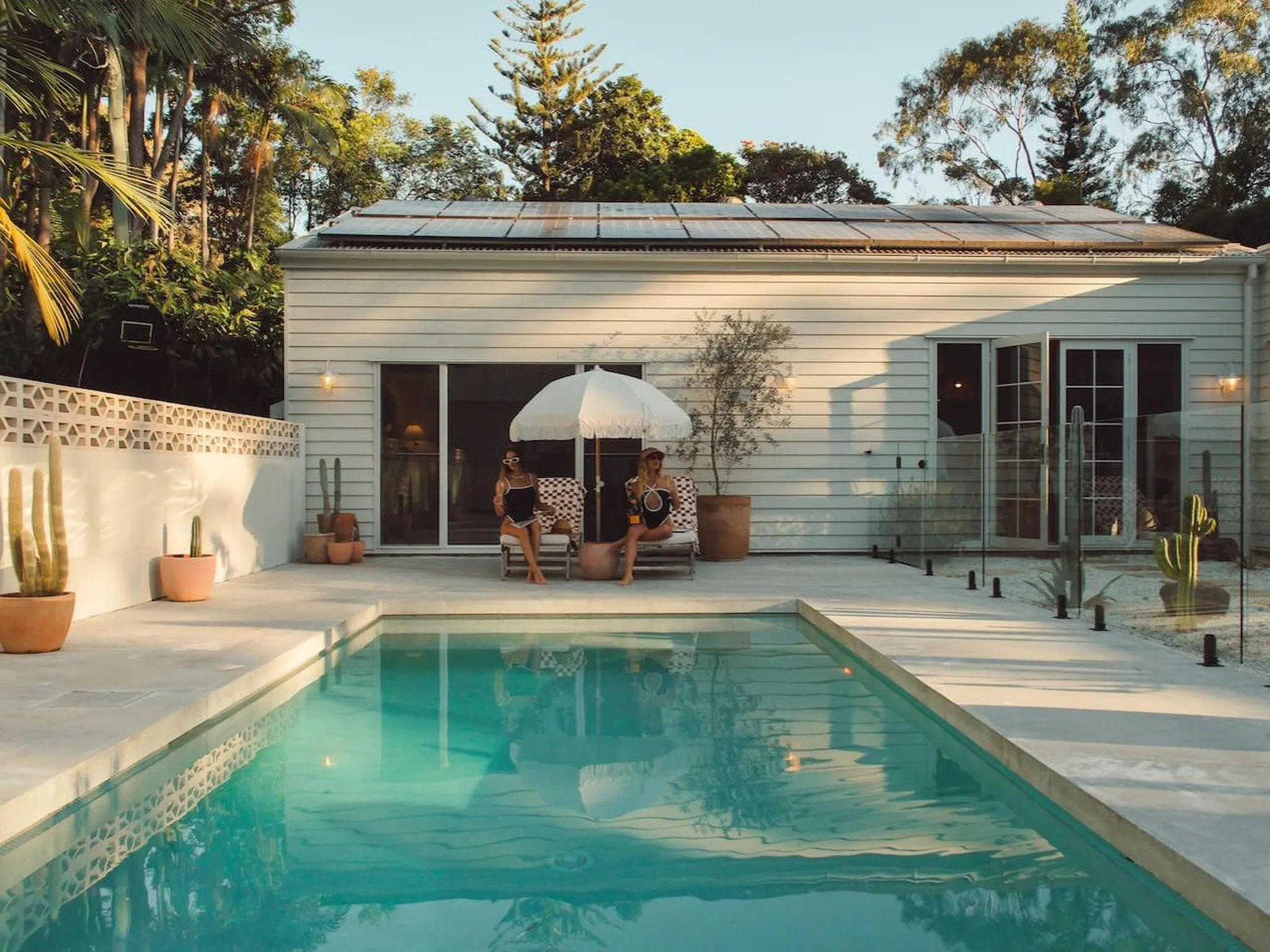 Two women relax by a pool under an umbrella.