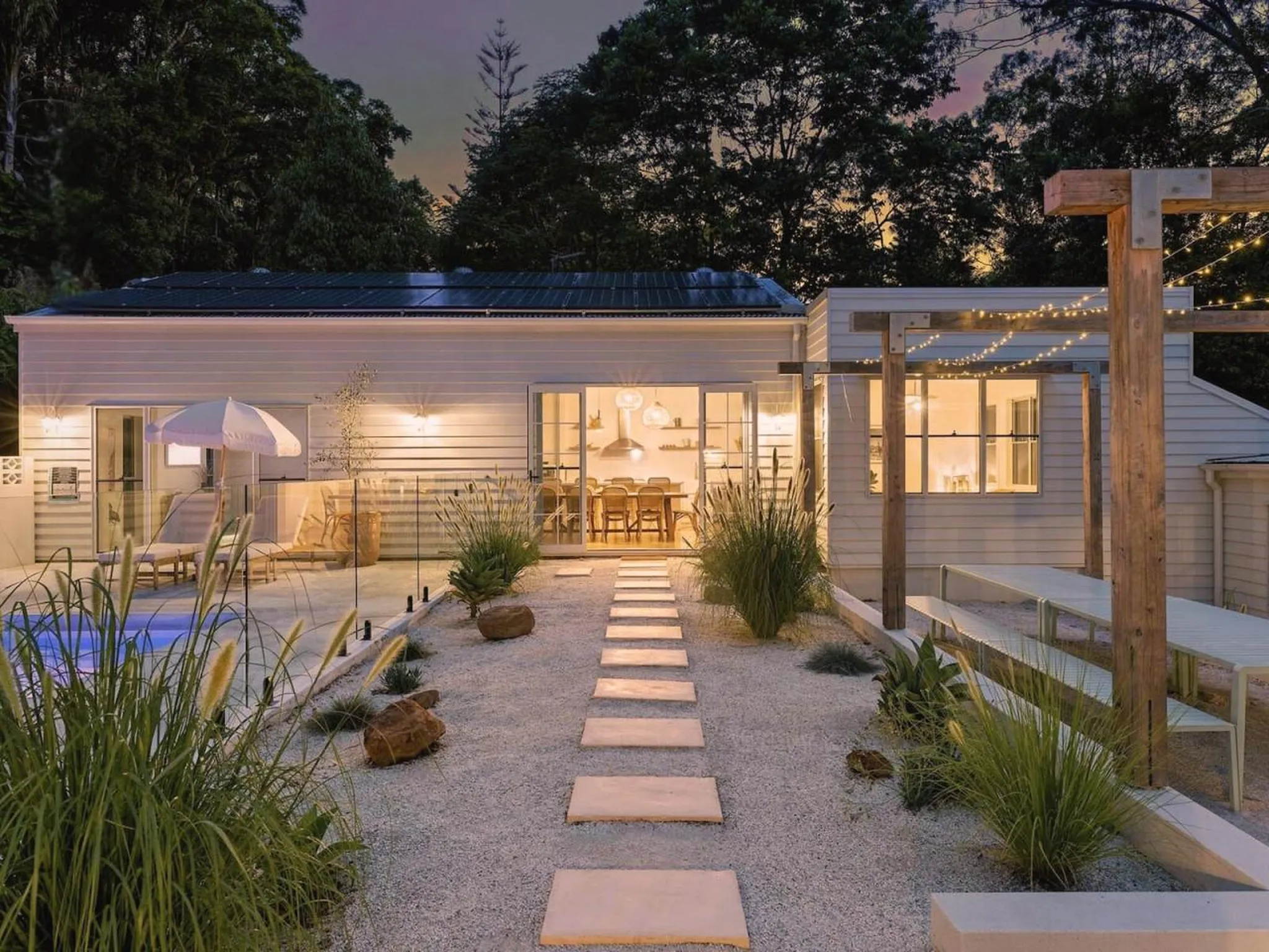 Modern house with solar panels, pool, and outdoor seating area illuminated by string lights.