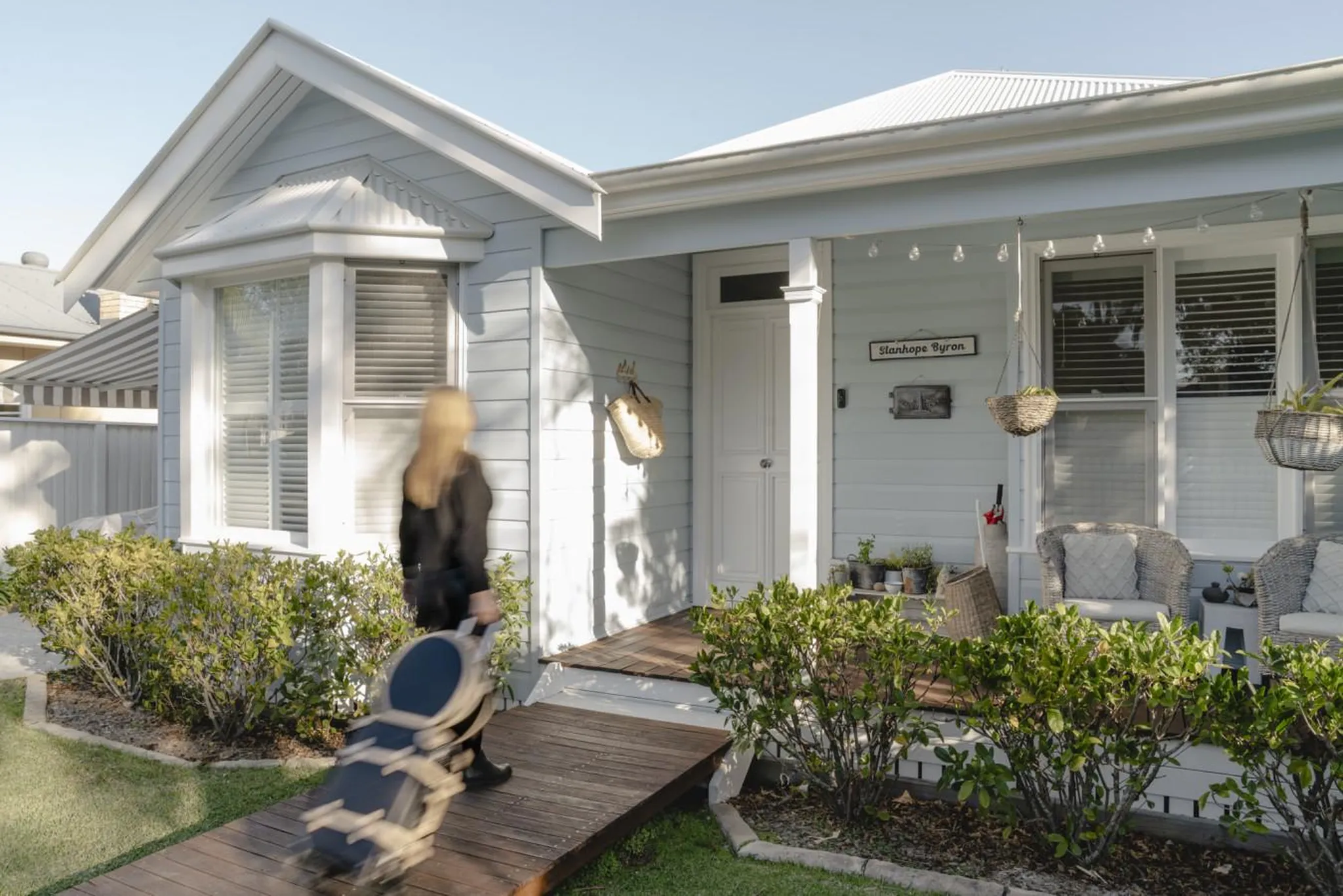 Woman with luggage walking up a ramp to a light blue house with a porch.