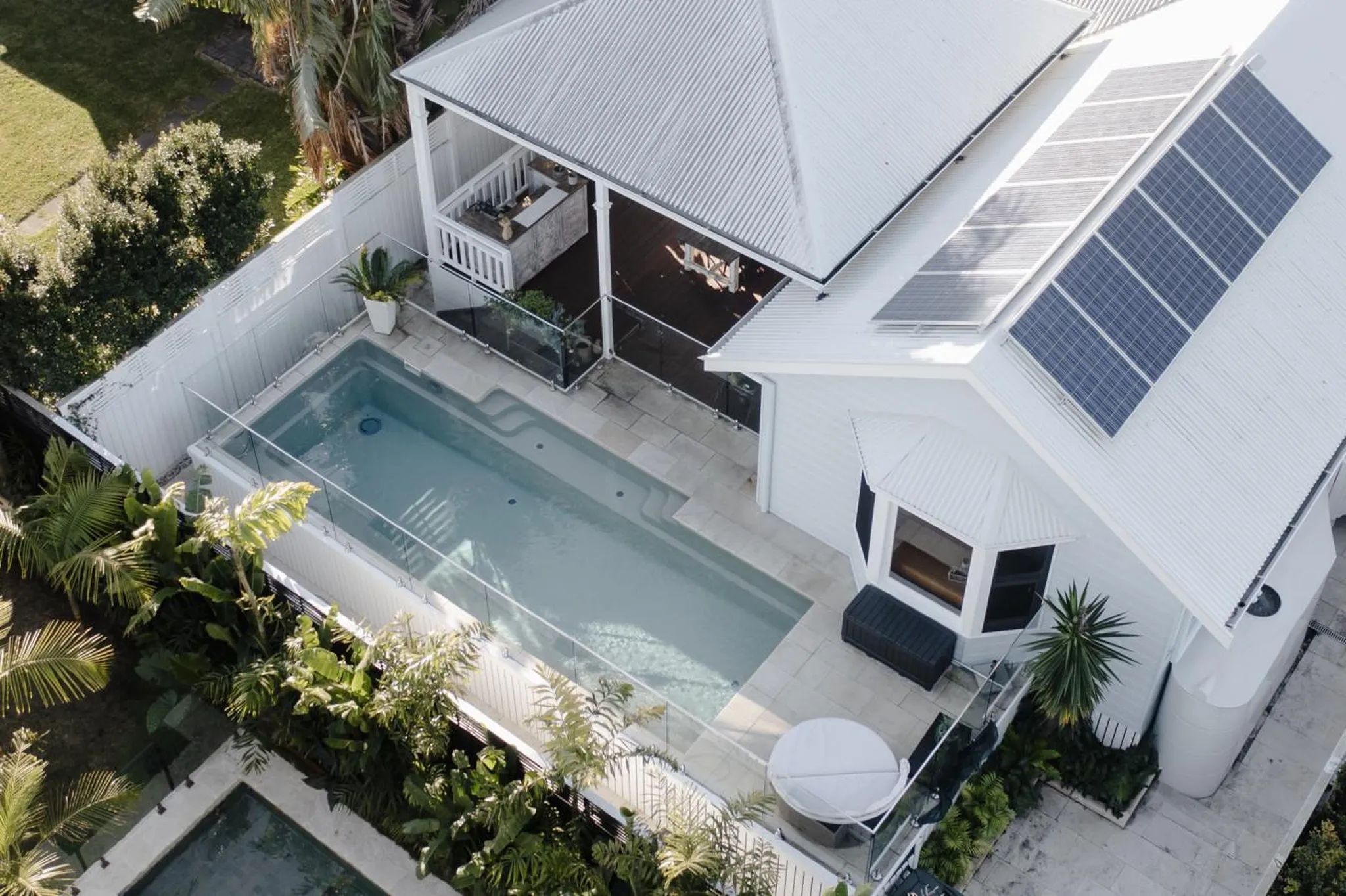 Aerial view of a modern white house with solar panels, a swimming pool, and lush tropical landscapin