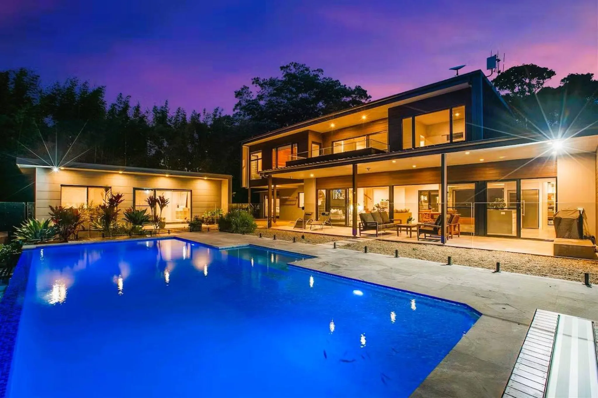 Luxury modern house with pool at dusk, featuring outdoor living space.