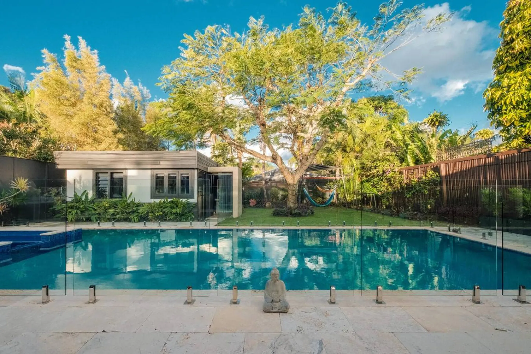 Buddha statue in front of a swimming pool with a modern building and lush greenery.