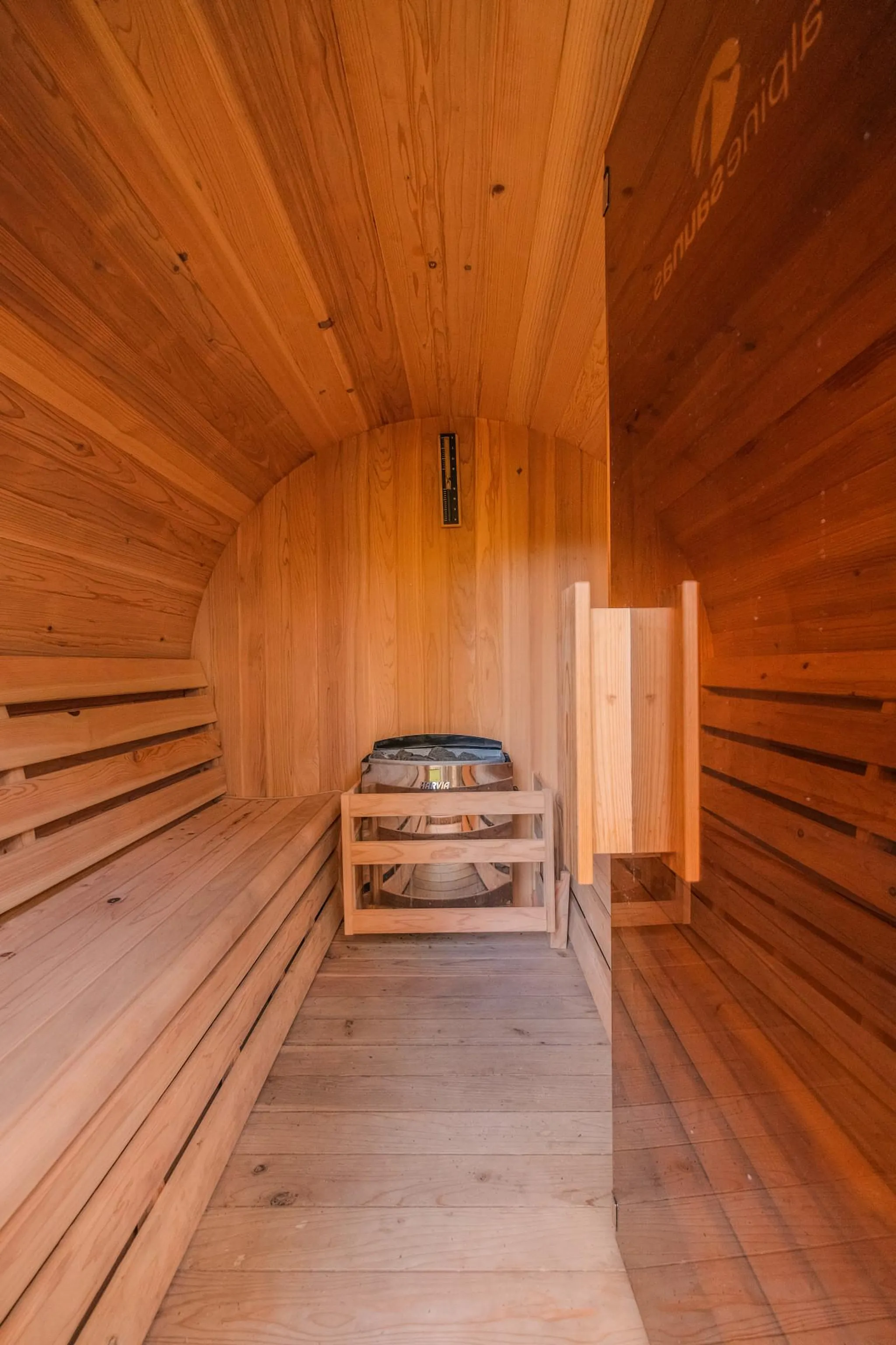Interior of a wooden sauna with benches, a heater, and a thermometer.
