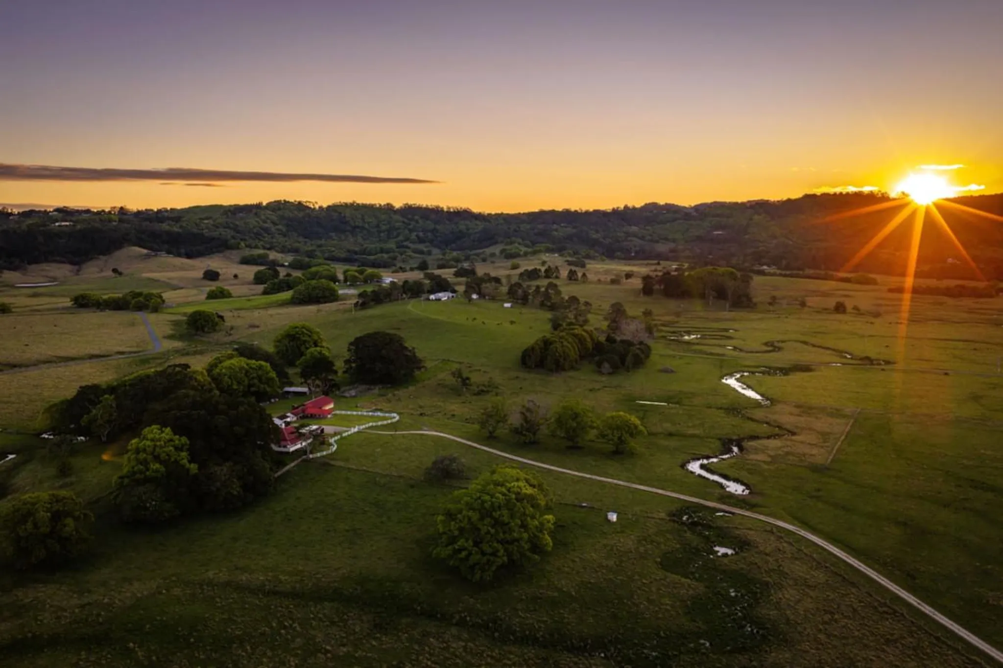 Rural landscape at sunset with rolling green hills, a winding river, and a farm.