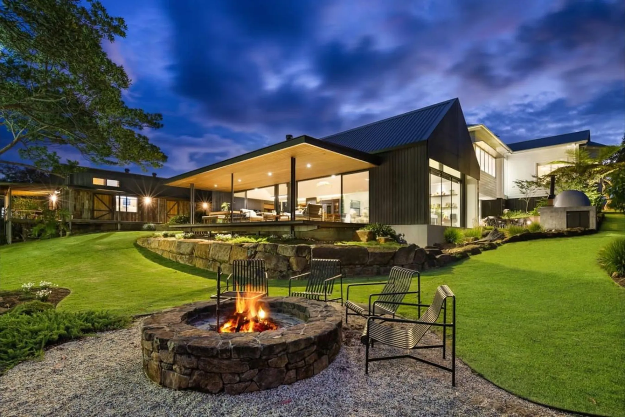Modern home with a fire pit and outdoor seating area at dusk.