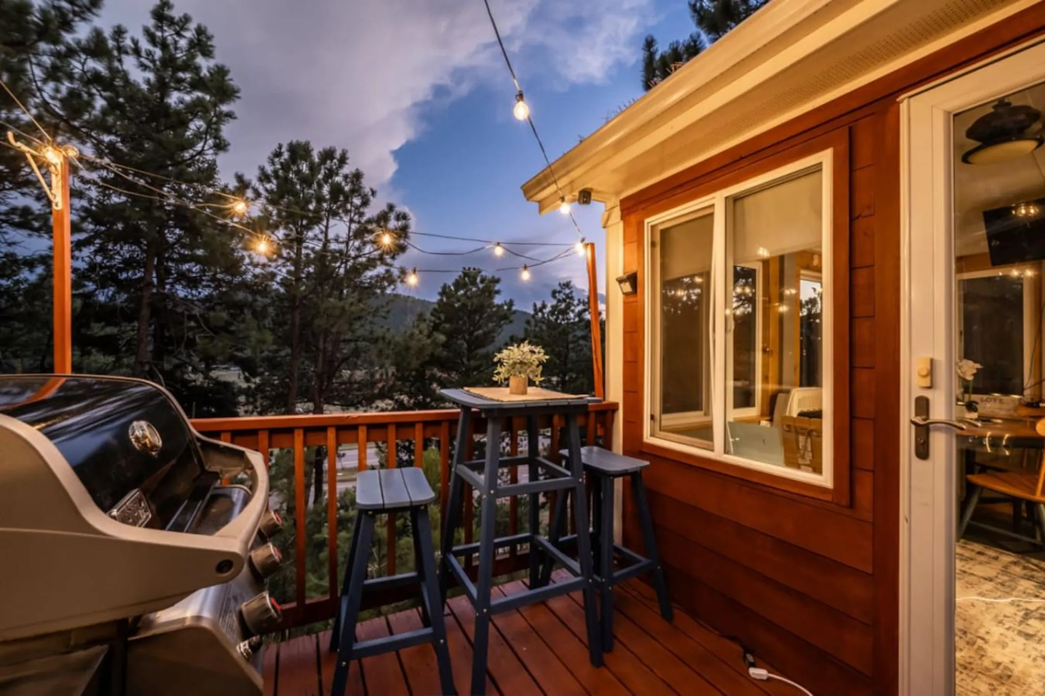 A deck with a grill, table, and stools at dusk.