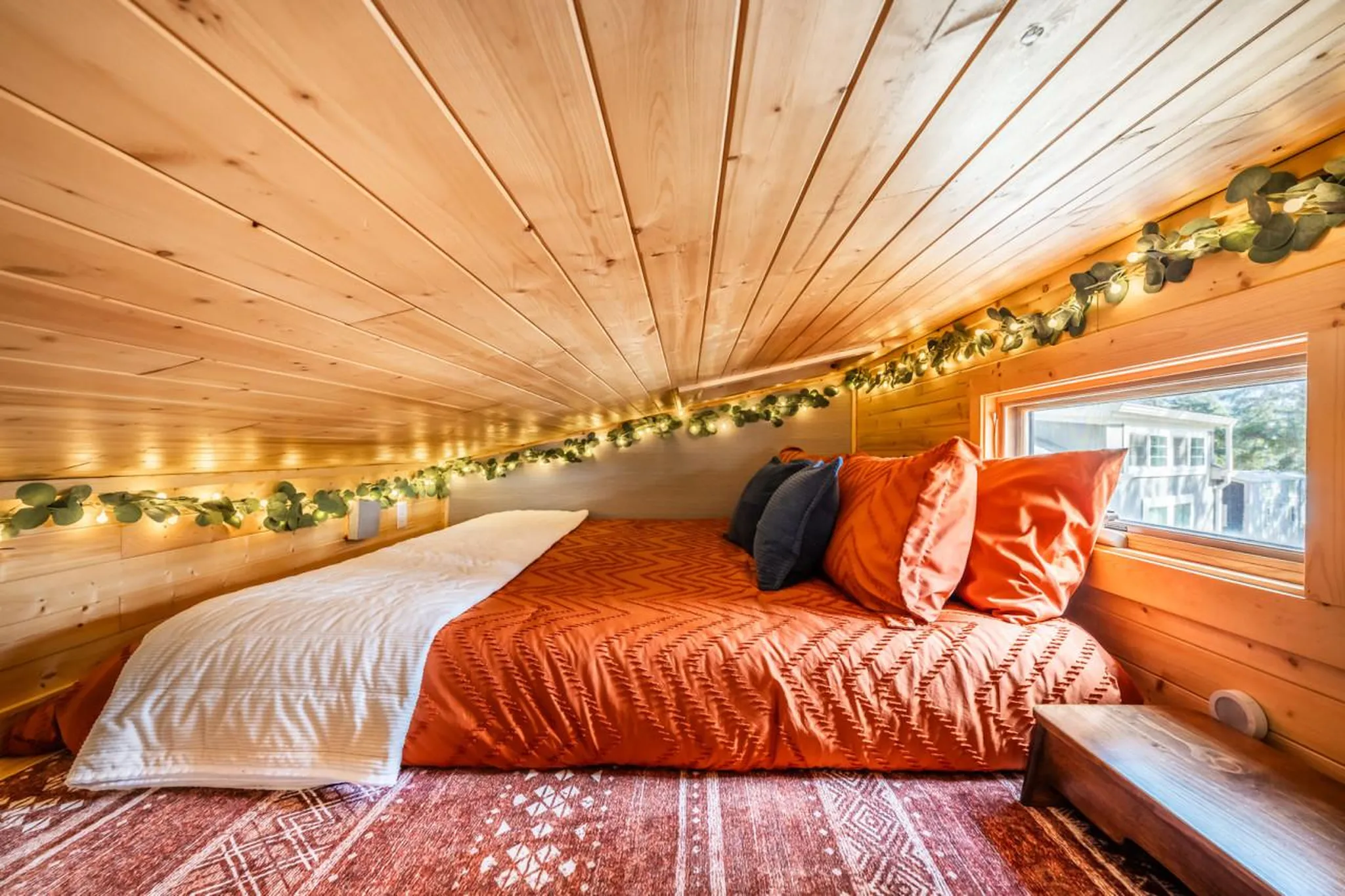 Cozy loft bedroom with a bed, orange bedding, and string lights.