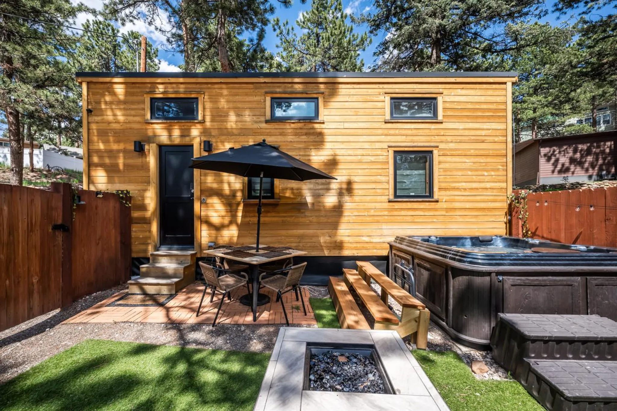 Backyard of a wooden tiny house with a hot tub, fire pit, and patio.