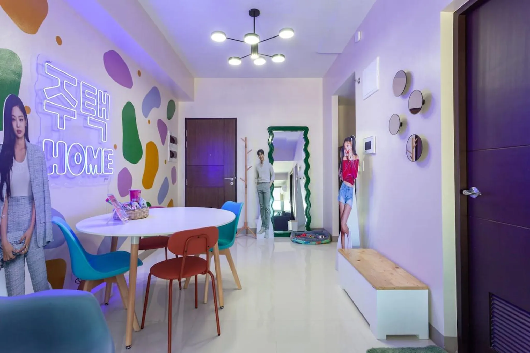 A brightly lit room with colorful walls, a white dining table and chairs, and cardboard cutouts of K
