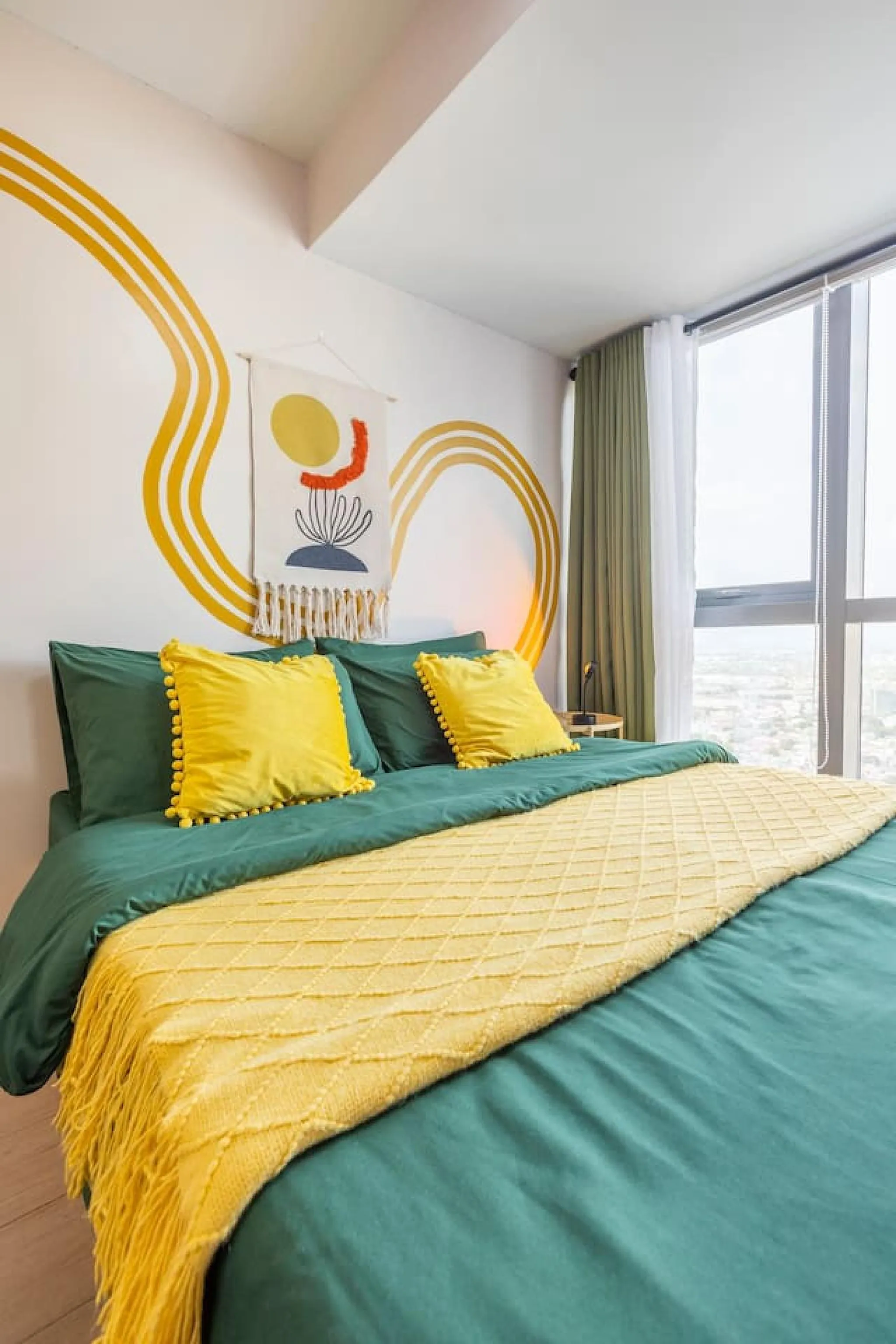 A bright, modern bedroom with a bed, yellow pillows, and a green comforter.