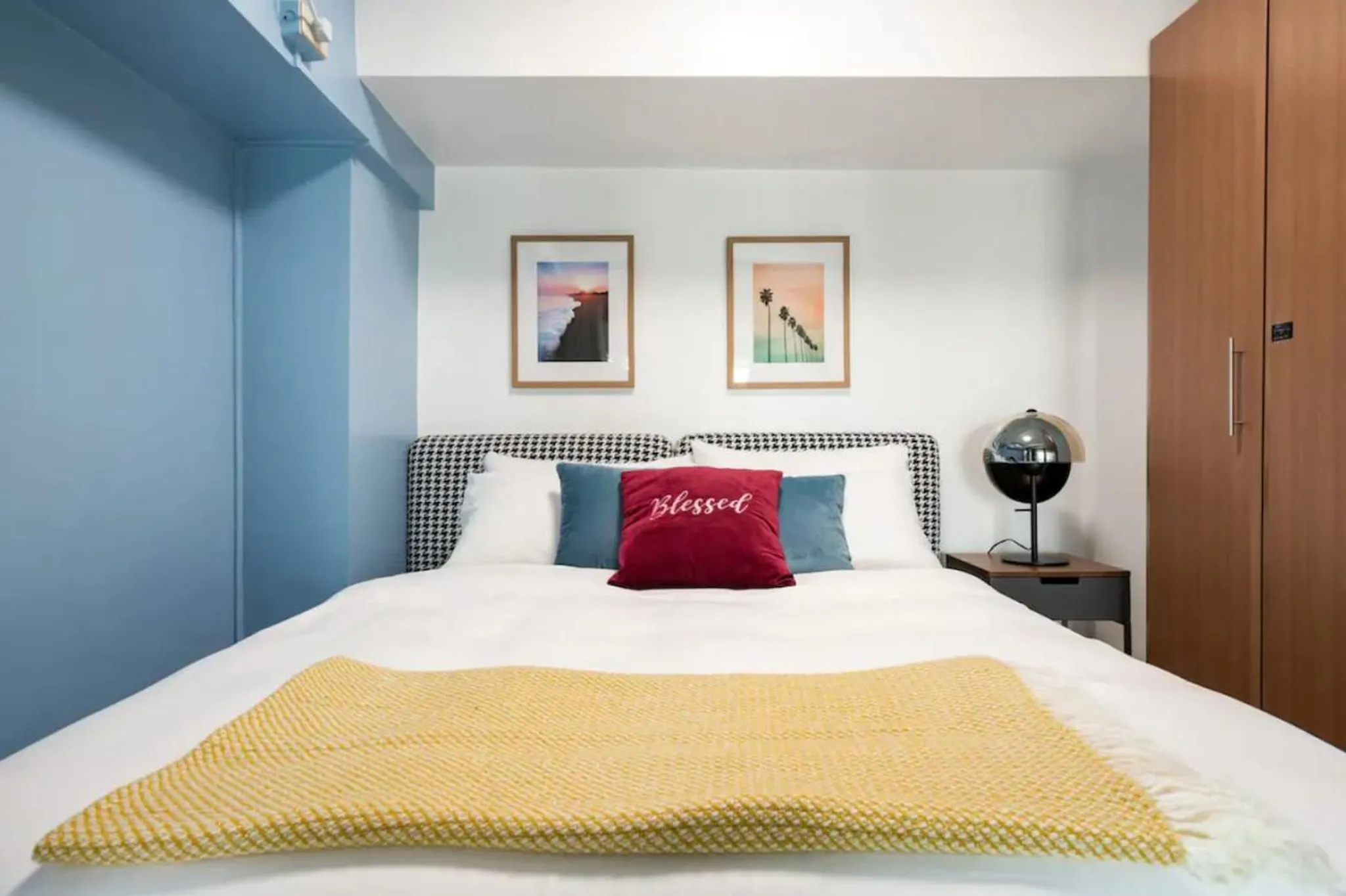 A bedroom with a bed, blue walls, two framed pictures, and a wardrobe.
