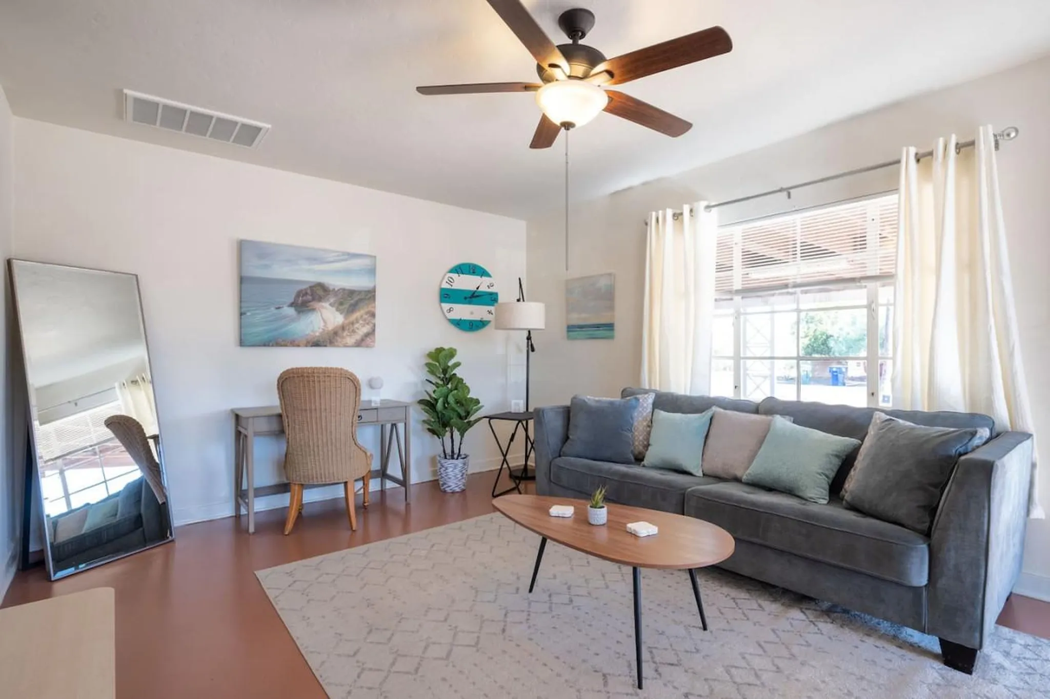 A living room with a grey couch, coffee table, and a desk with a chair.