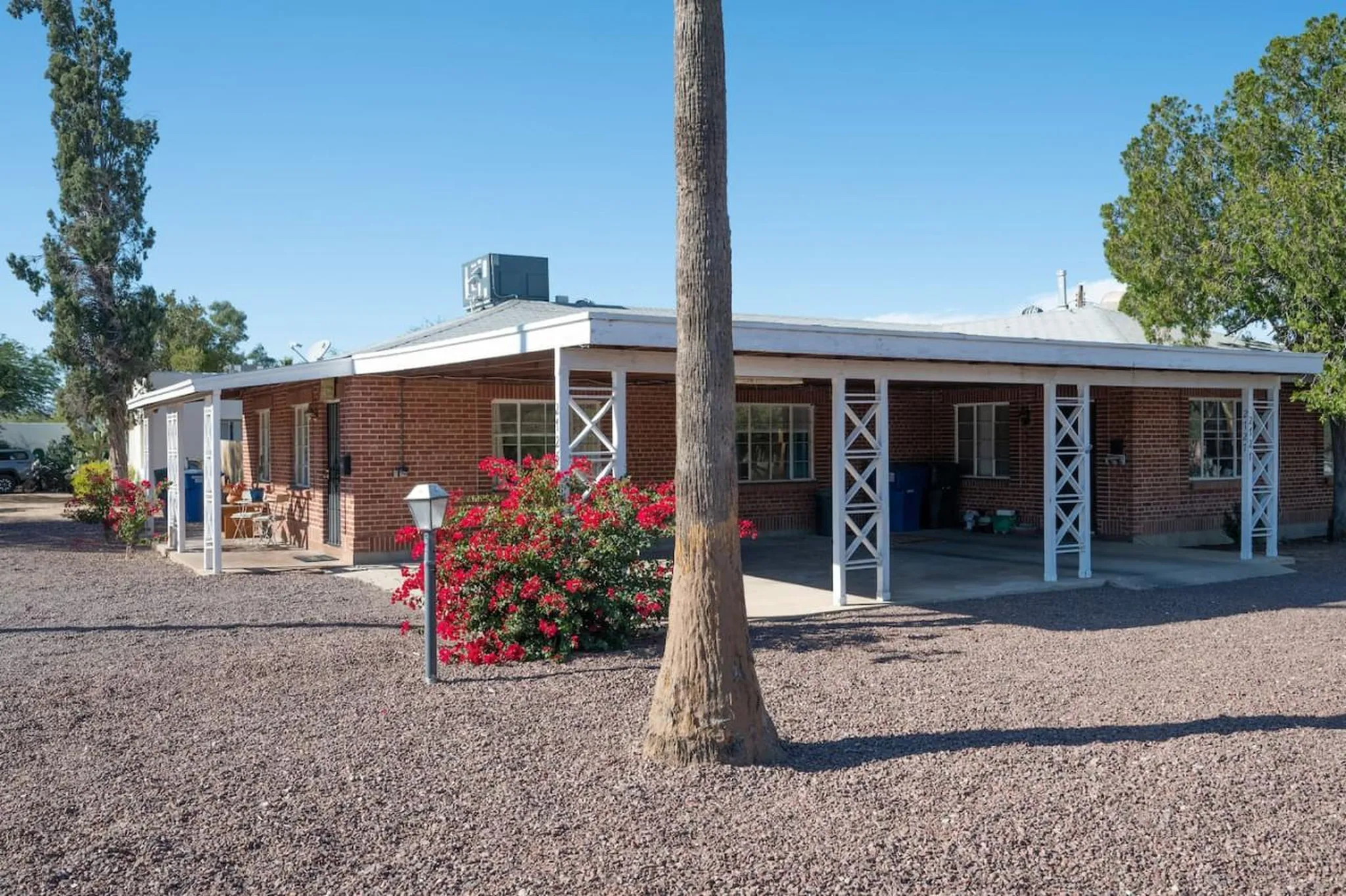 A ranch-style brick house with a covered patio and a palm tree in the foreground.