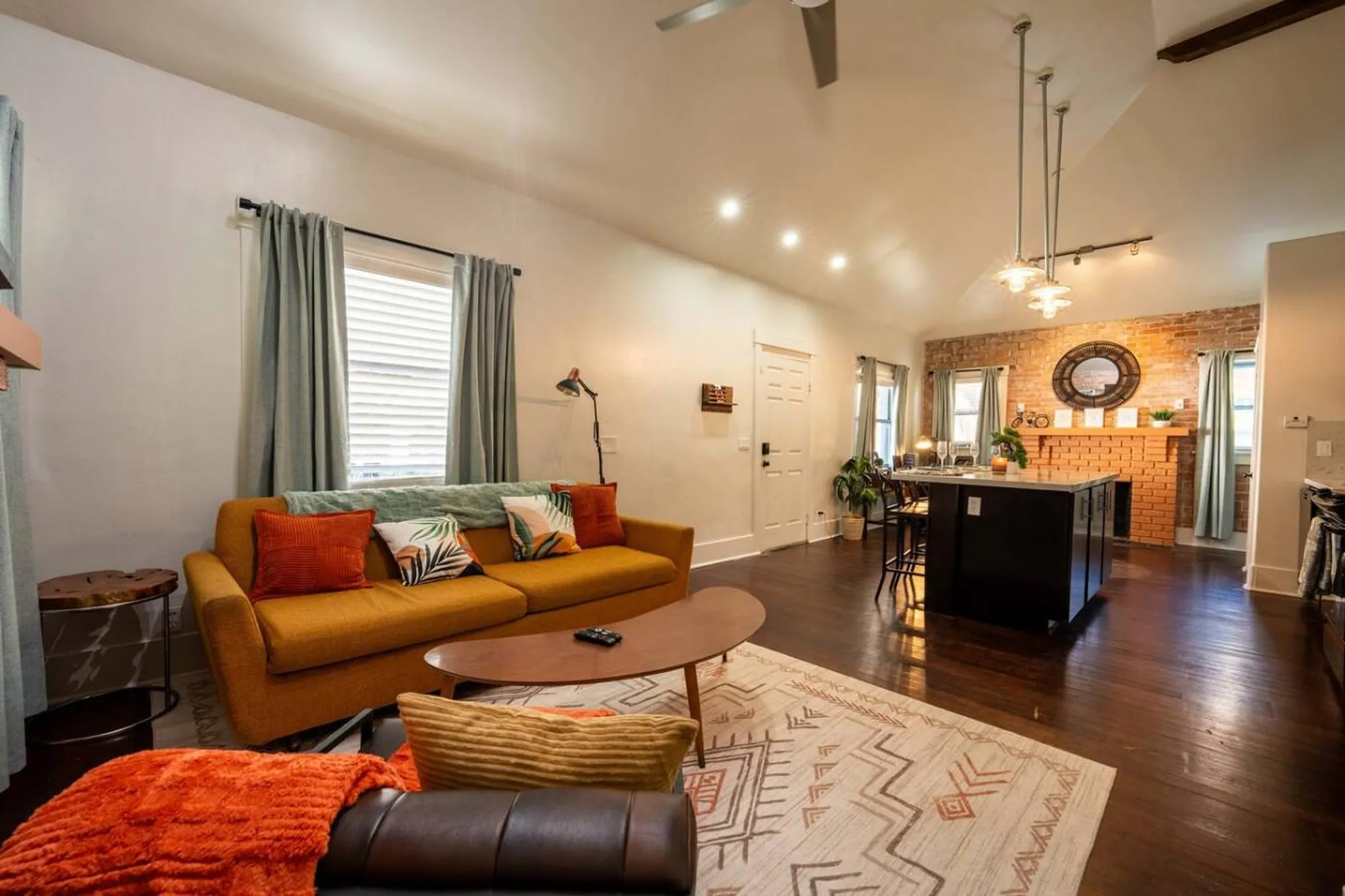 Cozy living room with a mustard yellow sofa, brick fireplace, and island kitchen.