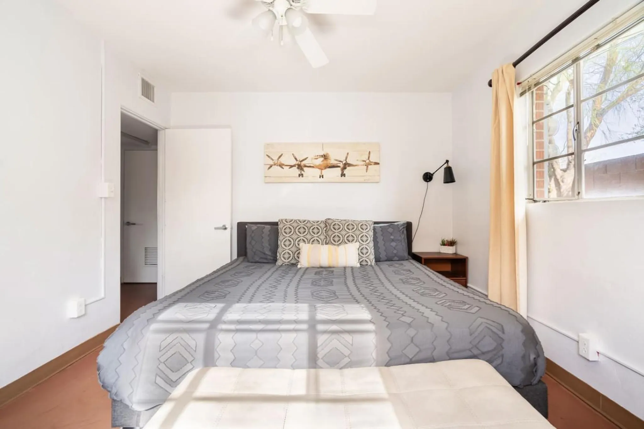 A bedroom with a bed, pillows, artwork, and a window with a curtain.