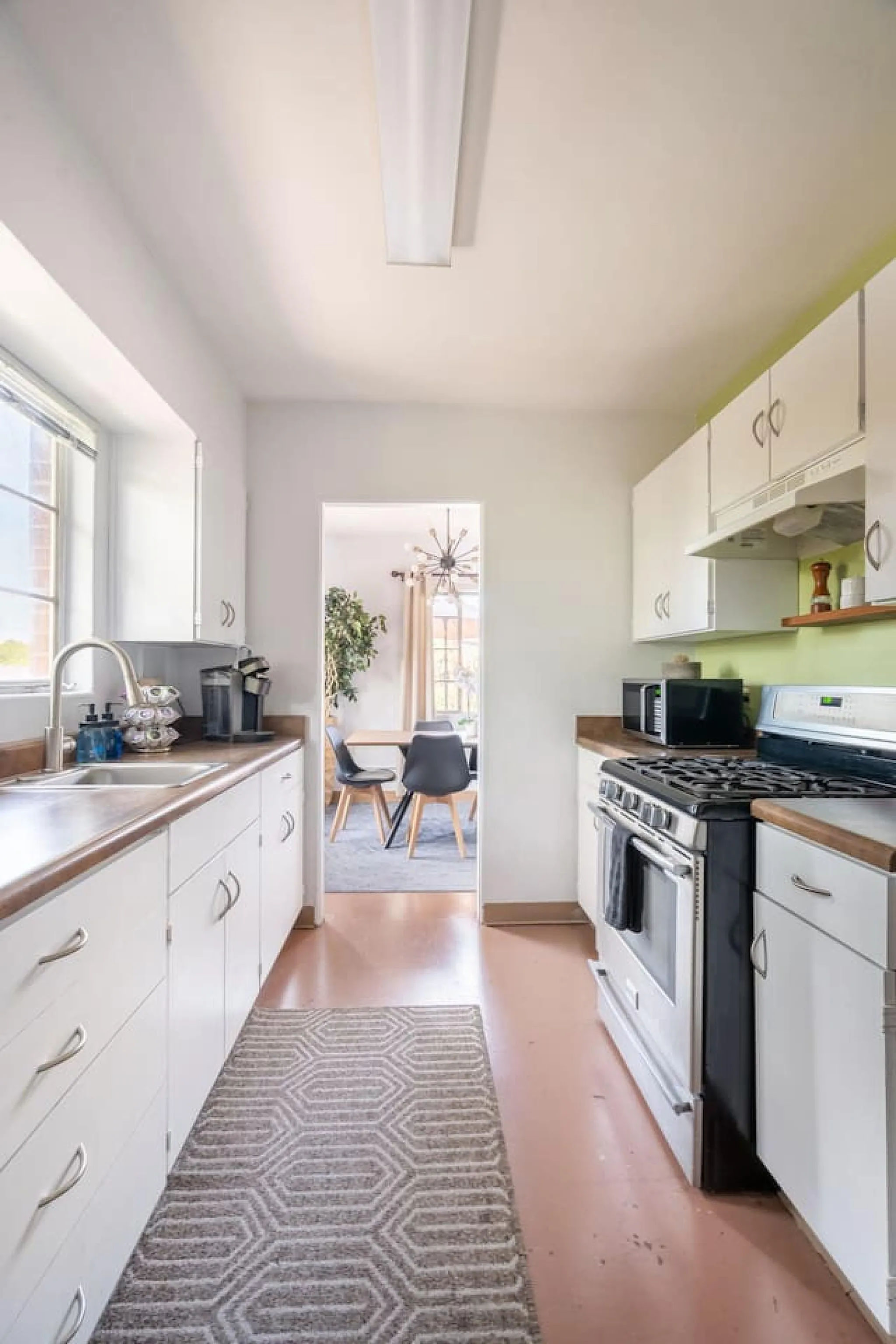 A galley kitchen with white cabinets, a stainless steel oven, and a pink floor.