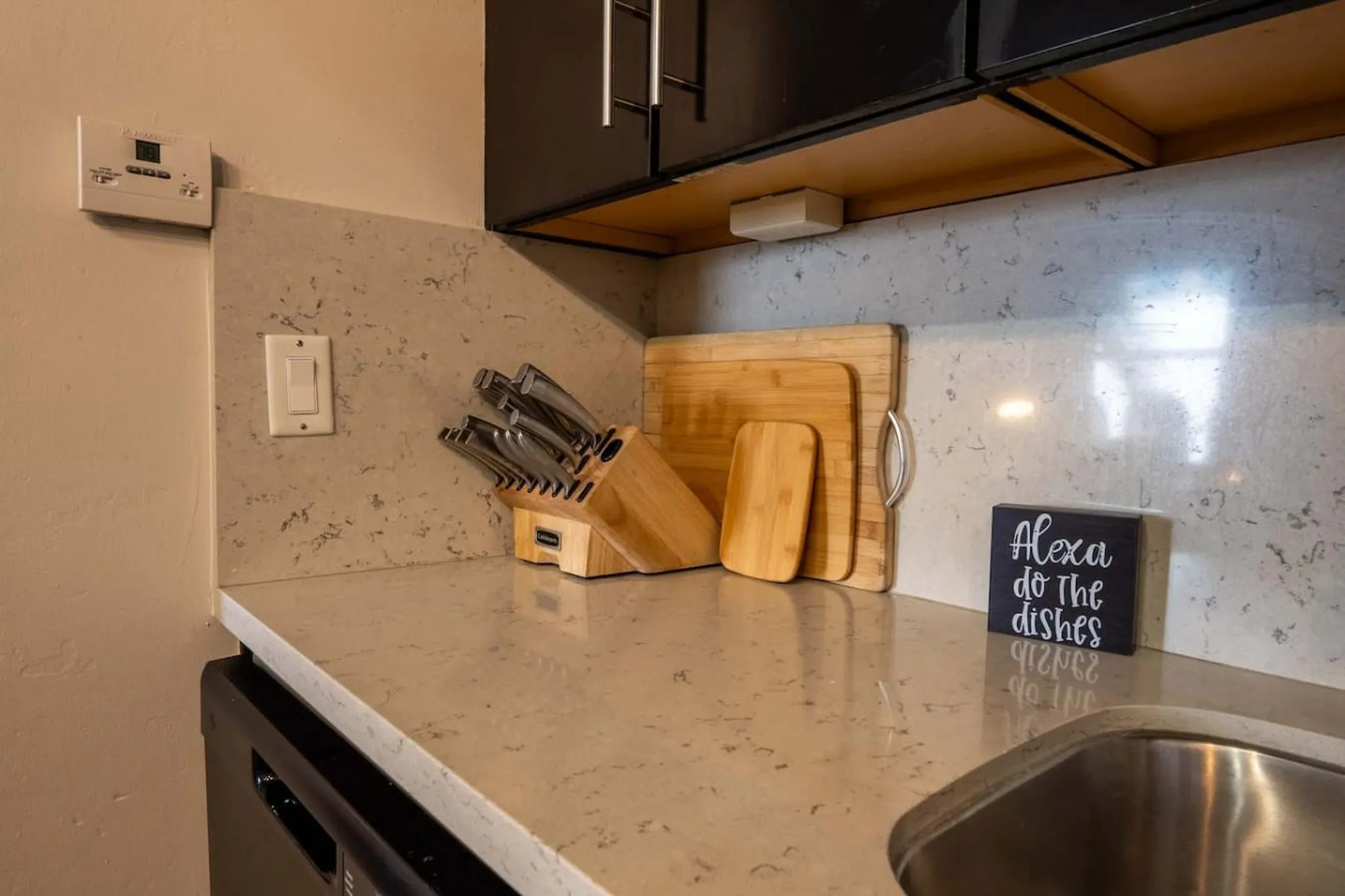A kitchen counter with a knife block, cutting boards, and a sign that says "Alexa do the dishes."