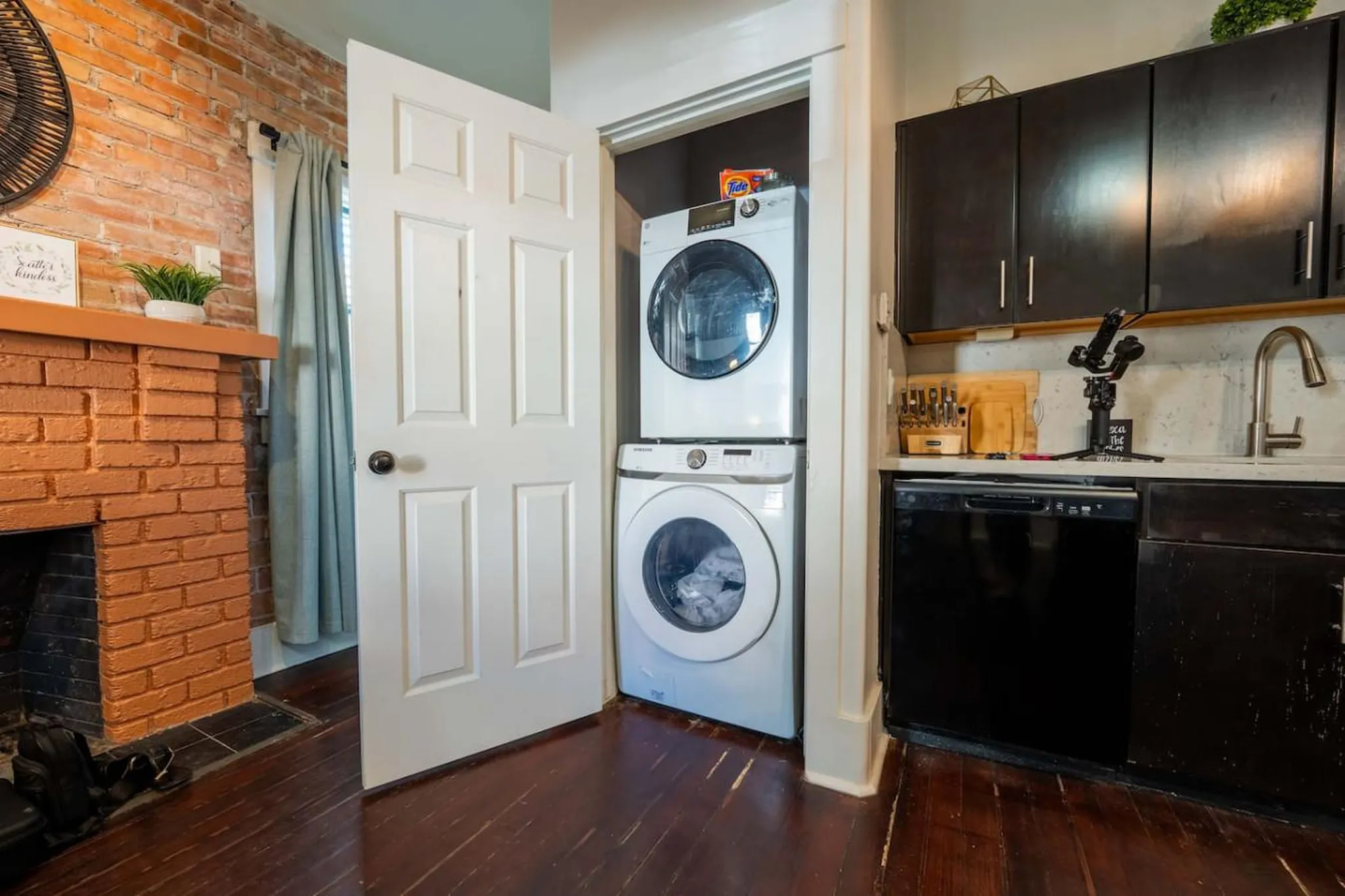 A kitchen with a stackable washer and dryer next to a fireplace and dark cabinets.